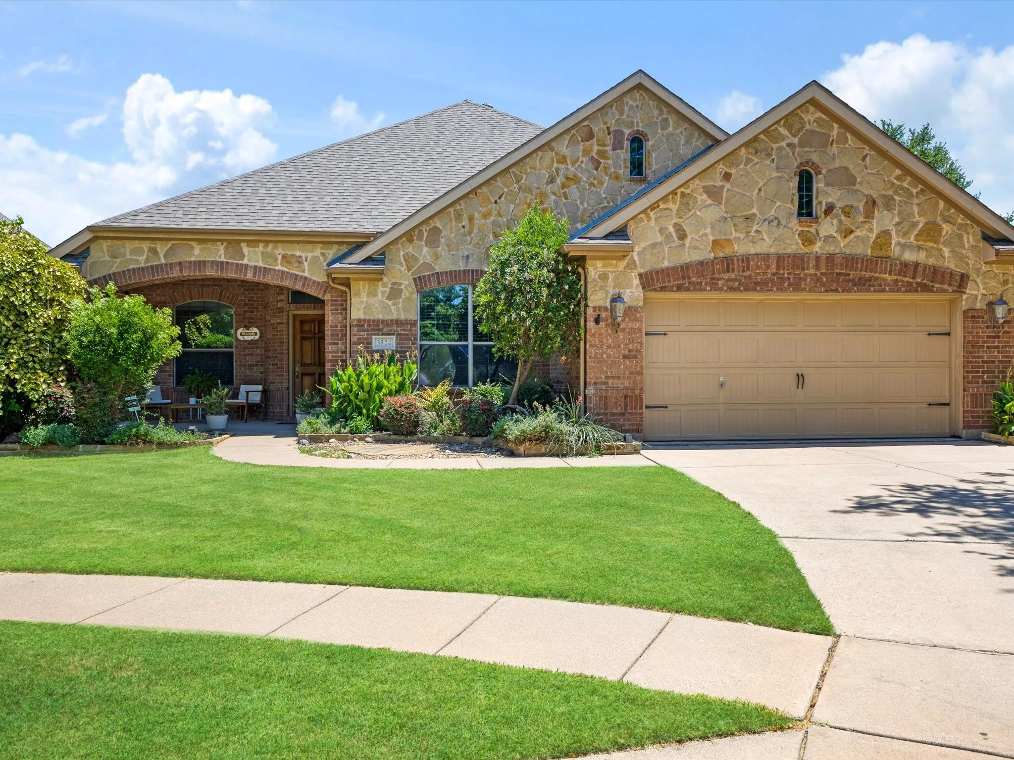 Stone and brick facade with arched entryway, covered front porch, and an attached two-car garage