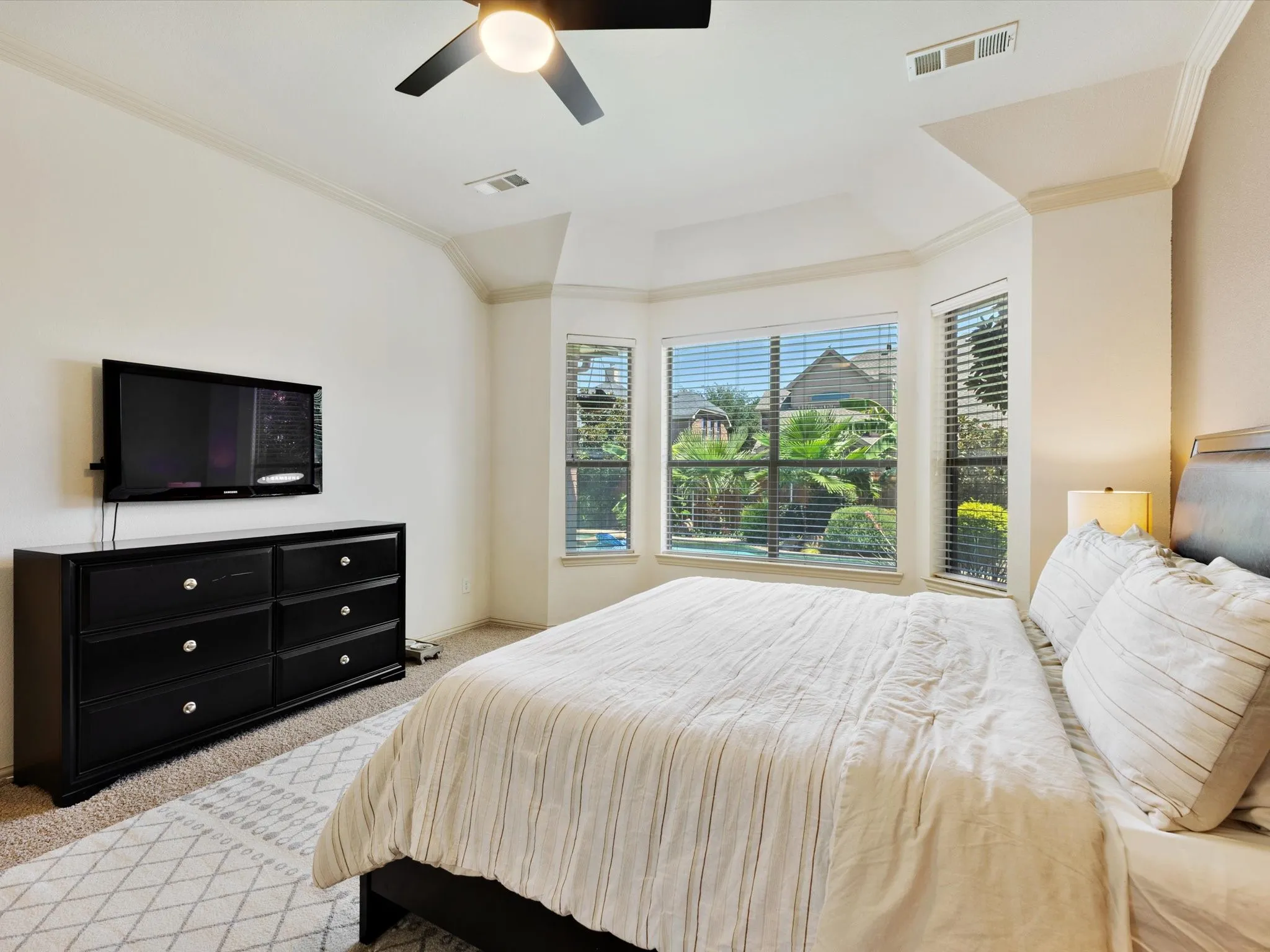 Bay window with multiple panels, ceiling fan with integrated lighting, recessed ceiling, crown molding, and carpeted flooring