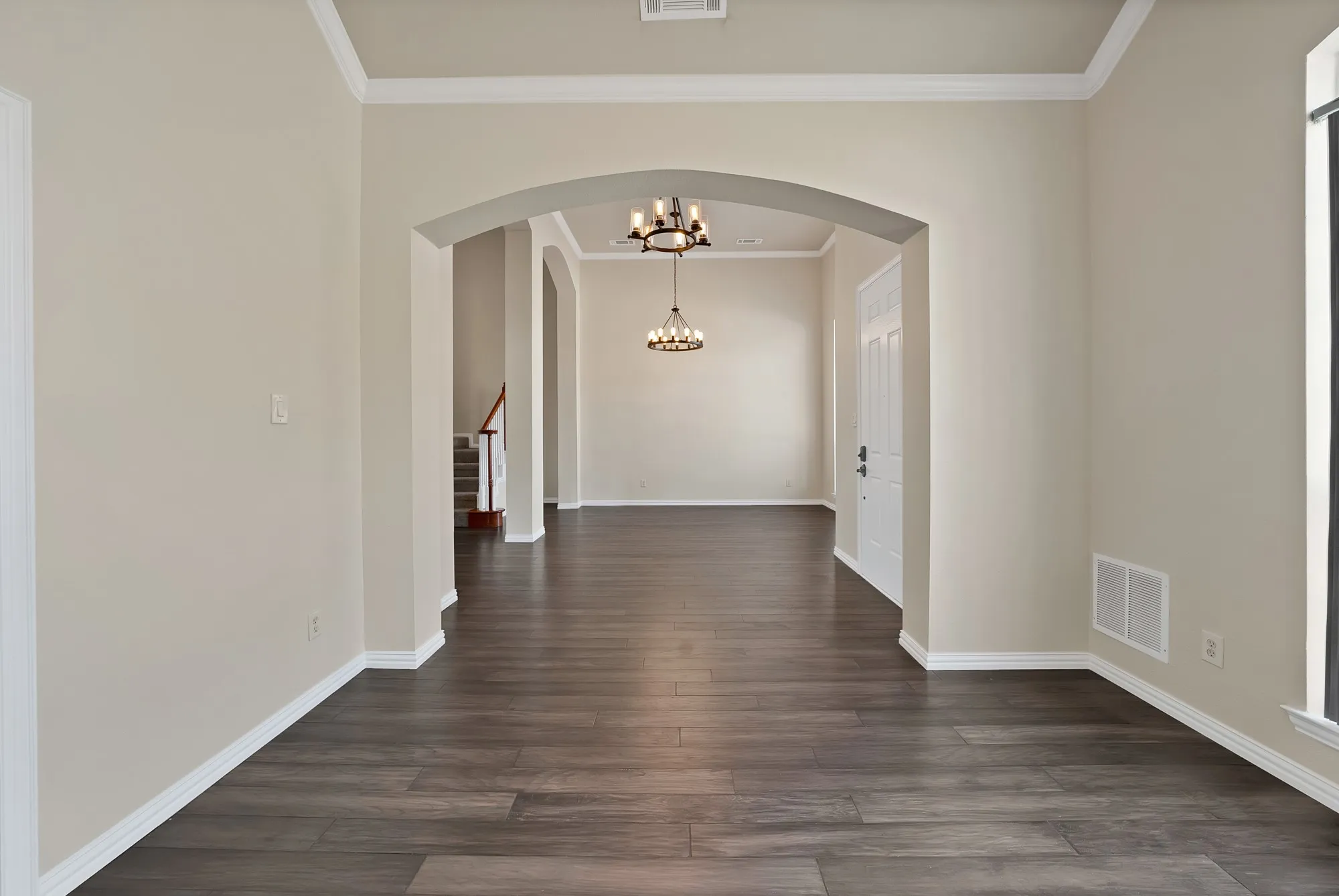 Wood-finish flooring throughout, framed by arched doorways, crown molding, and neutral wall tones