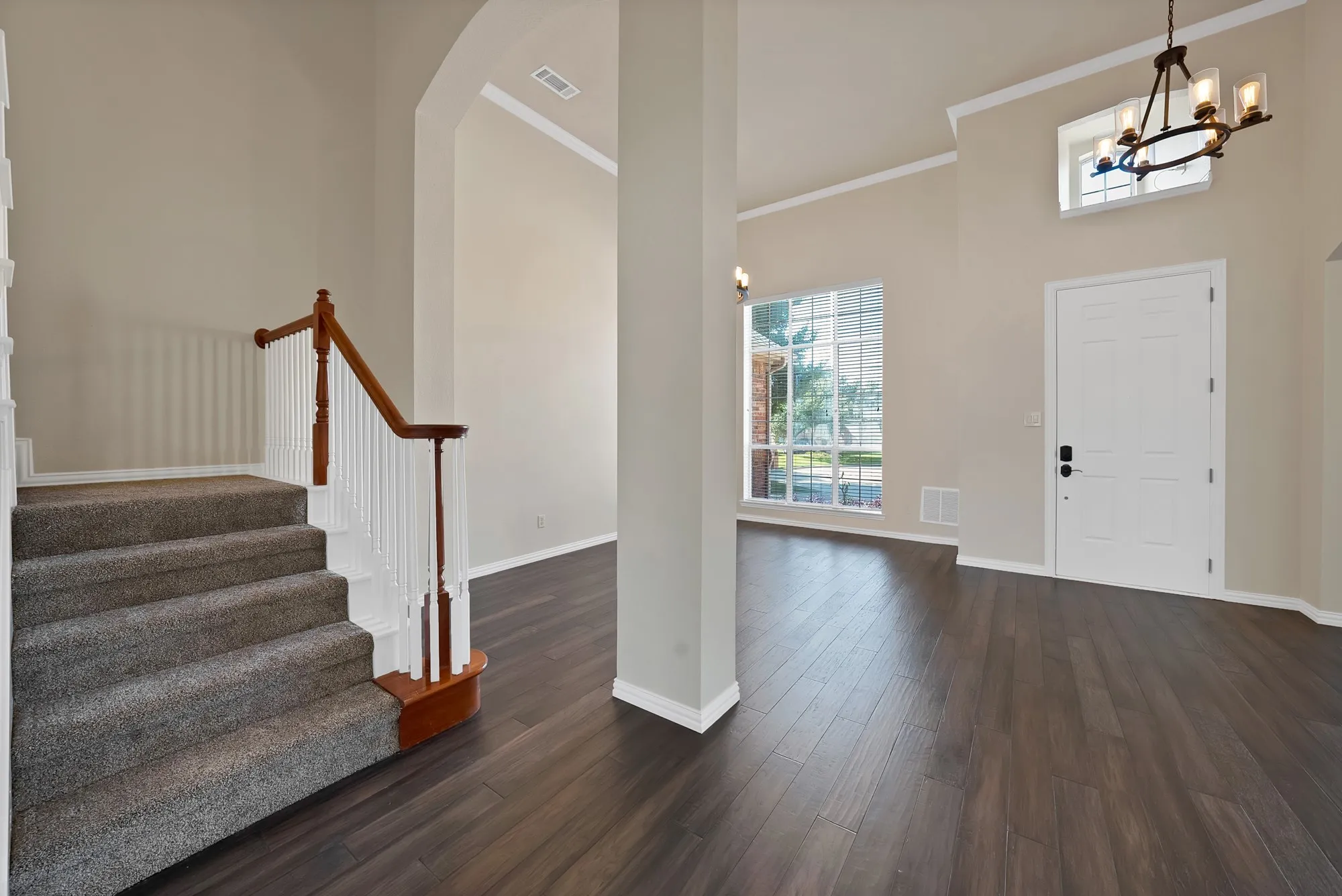 High ceilings and expansive windows in this entry foyer, featuring dark wood-finish flooring and a carpeted staircase with a wood and white spindle railing