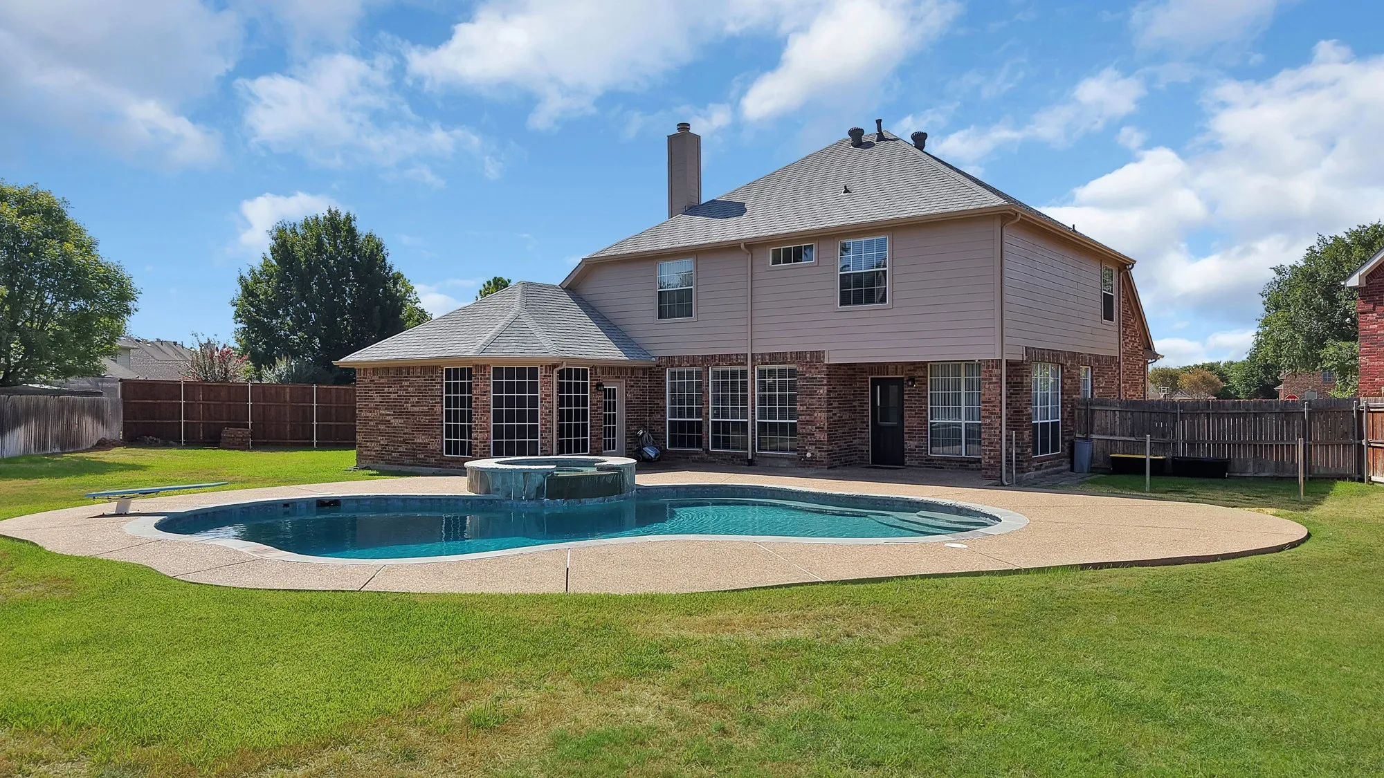Spacious backyard featuring a large in-ground swimming pool with an attached spa, expansive concrete decking, and a brick and siding exterior