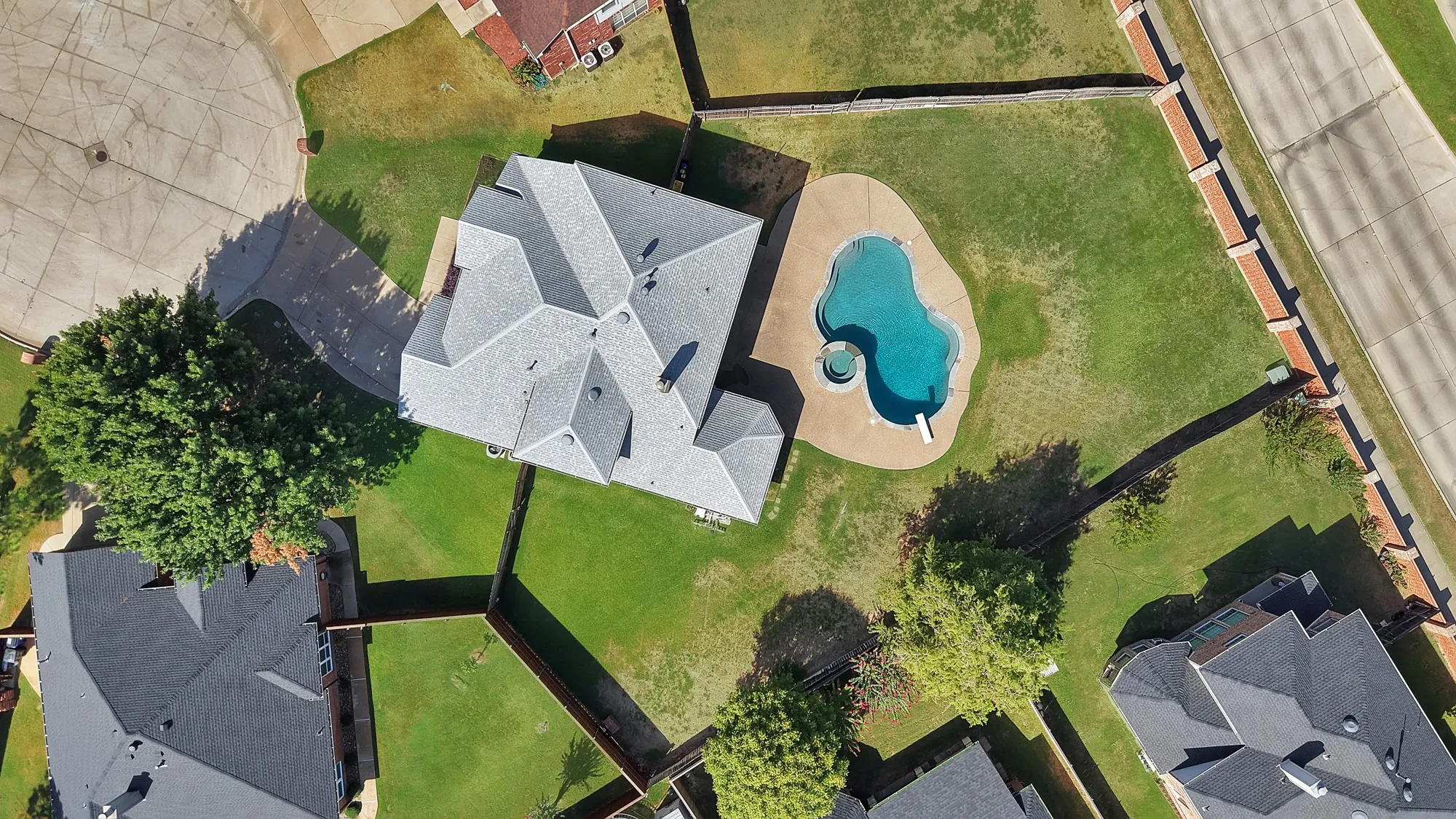 Expansive property featuring a multi-gabled roof, mature trees, a curvilinear swimming pool, and a dedicated spa