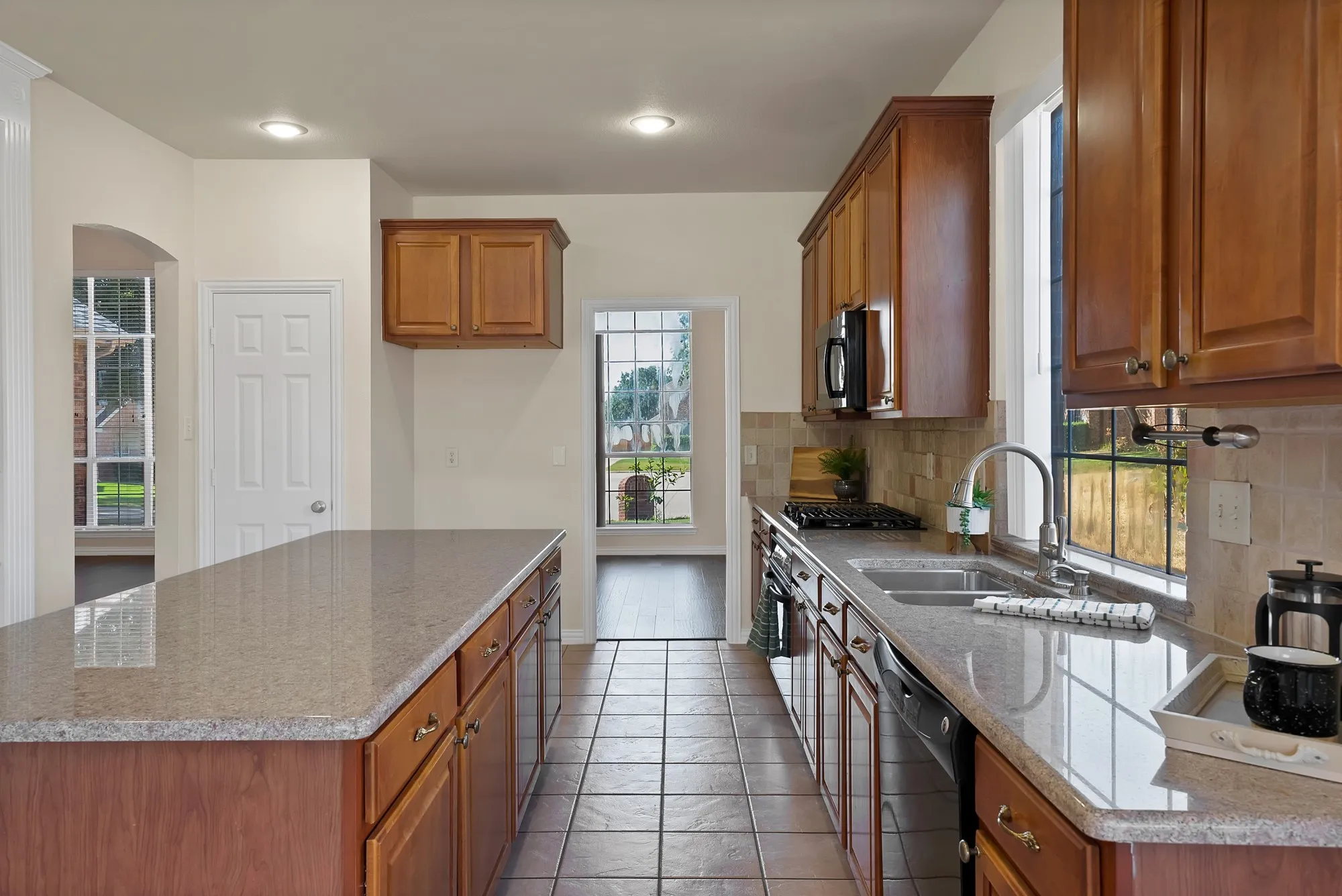 Kitchen featuring an expansive island with stone countertops, wood cabinetry, a stainless steel sink, and tile flooring