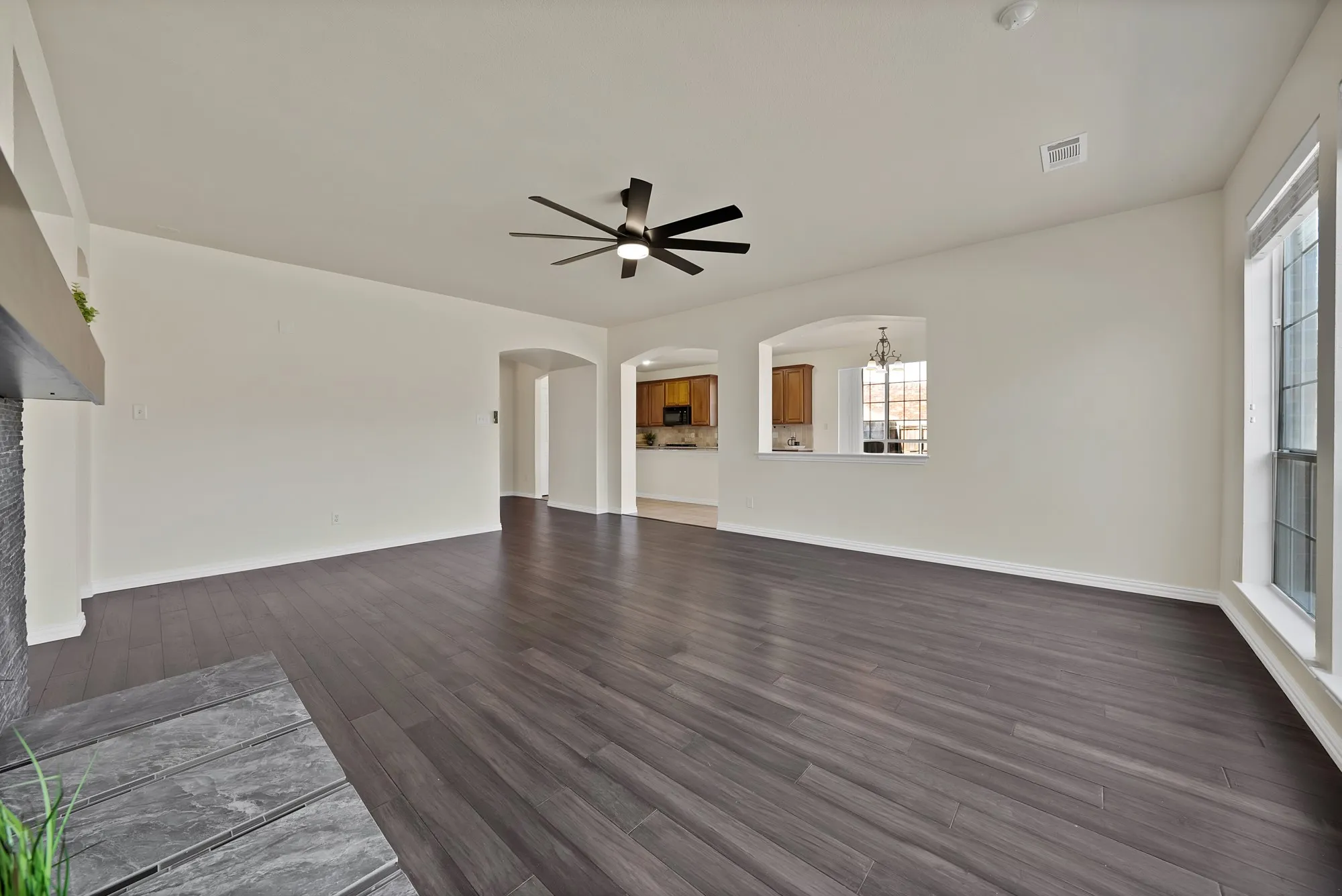 Wood-finish flooring, recessed ceiling fan, white trim windows, arched doorways, and a fireplace with a stone-finish hearth