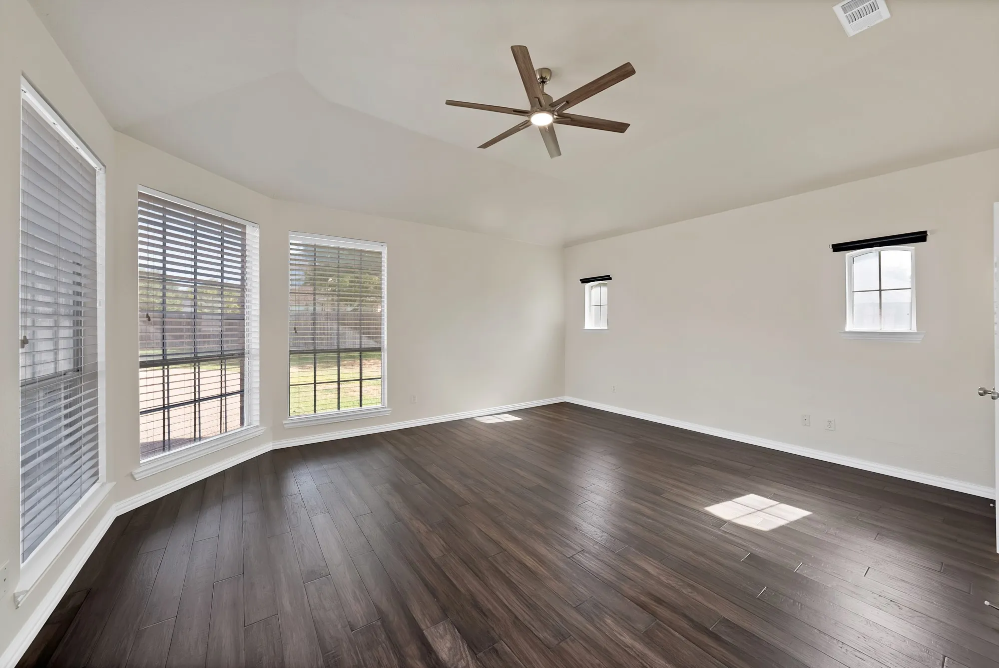 Spacious room featuring wood-finish flooring, a contemporary ceiling fan, and multiple windows with horizontal blinds