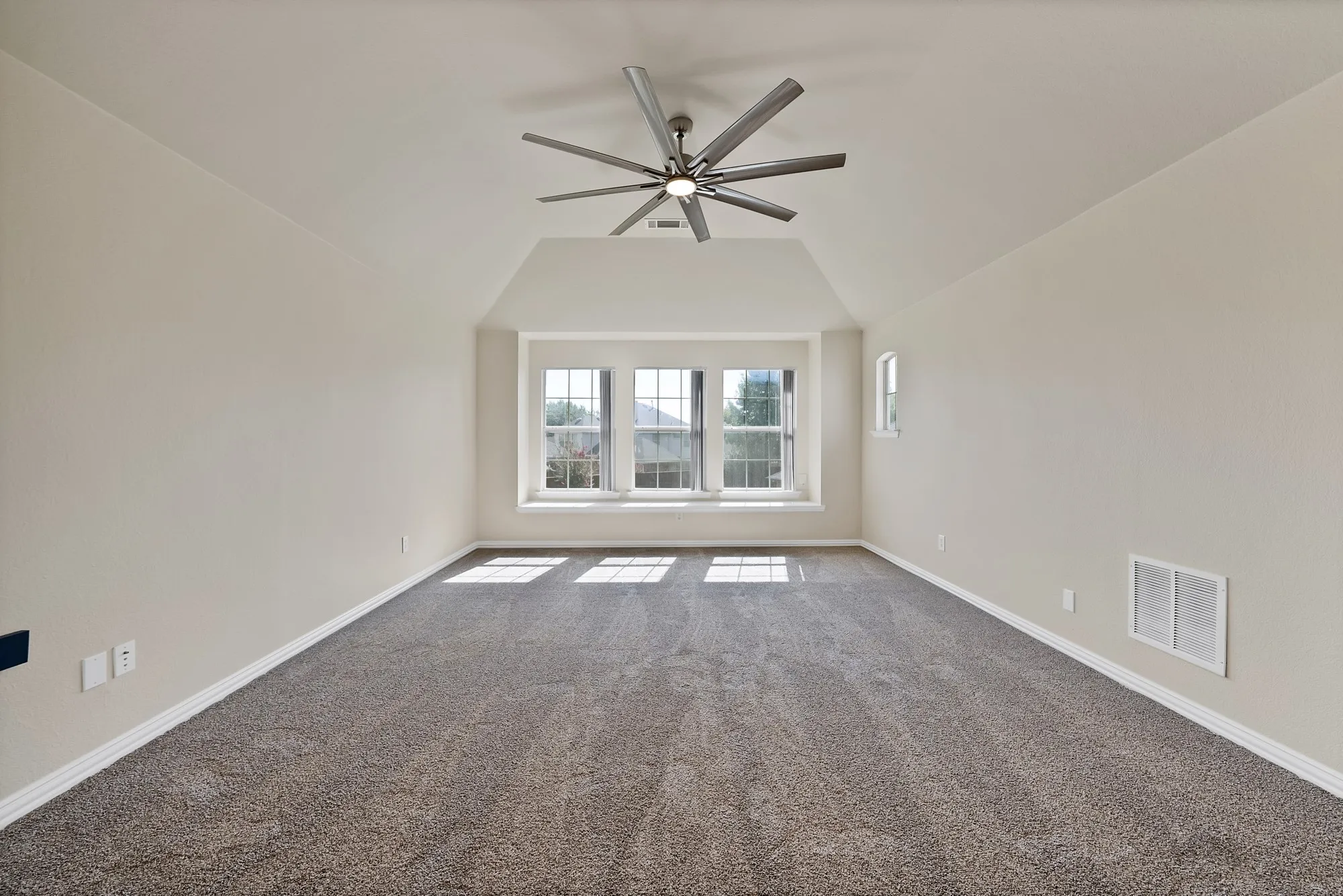 Spacious carpeted room featuring a wide window seat, vaulted ceiling, and a contemporary ceiling fan with integrated lighting