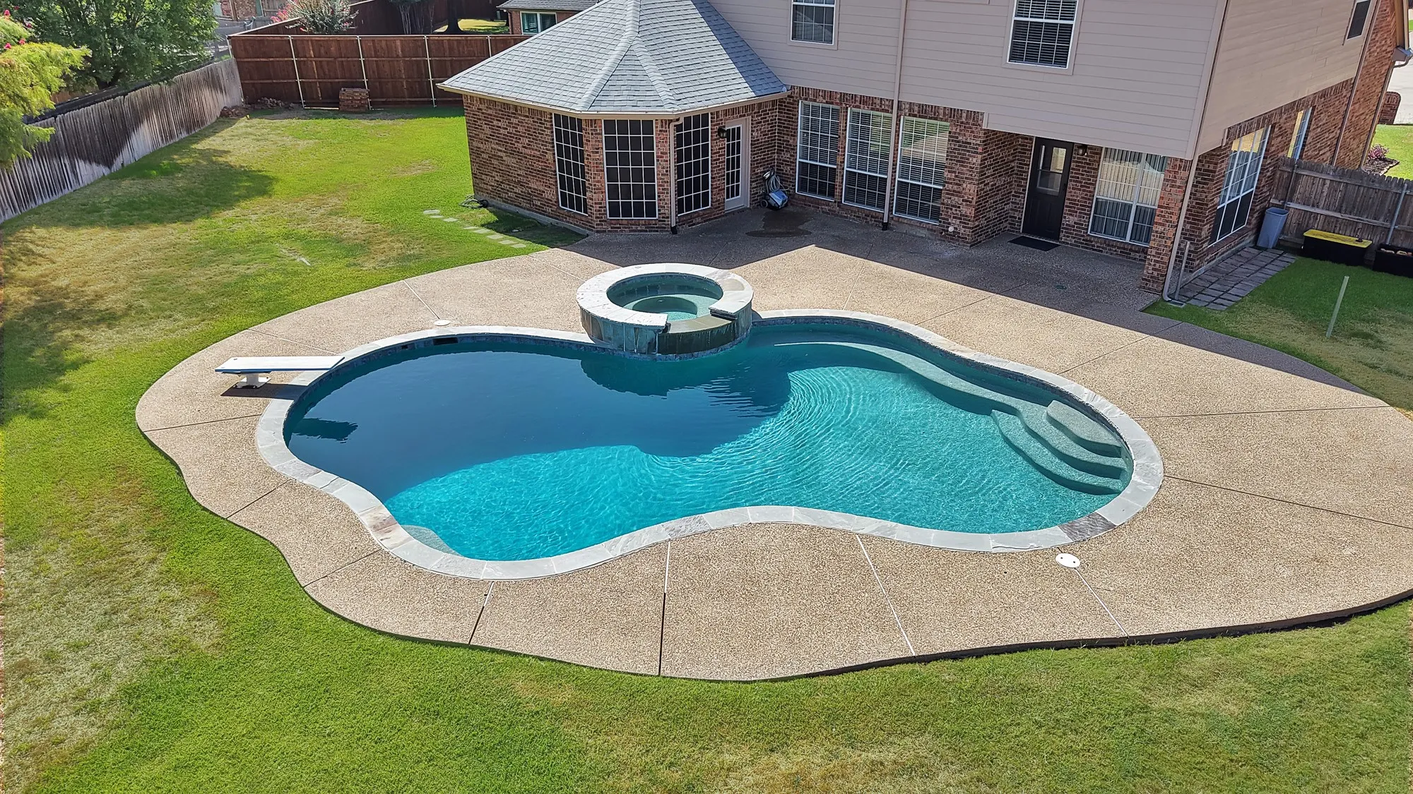 Expansive backyard featuring a freeform swimming pool with integrated spa and waterfall, a diving board, and an exposed aggregate patio