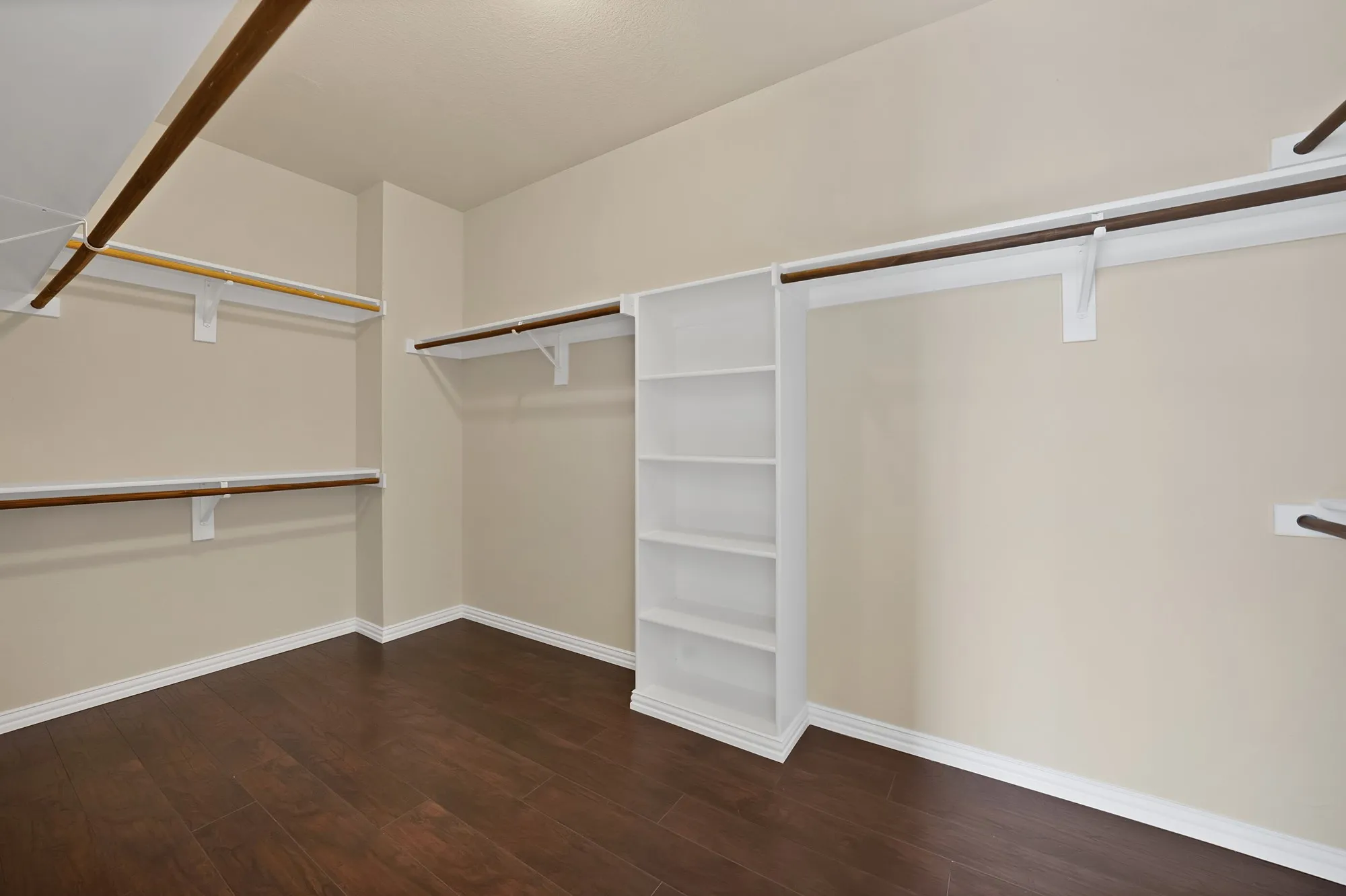 Spacious closet featuring wood-finish flooring, built-in shelving, and multiple hanging rods