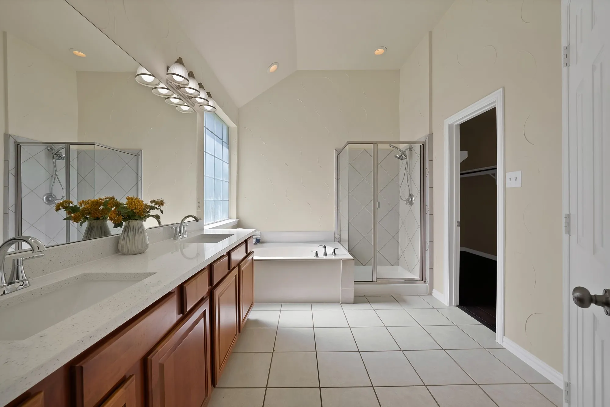 Dual vanity with integrated sinks and chrome fixtures, wood-finish cabinetry, built-in soaking tub, glass-enclosed shower, and tile flooring