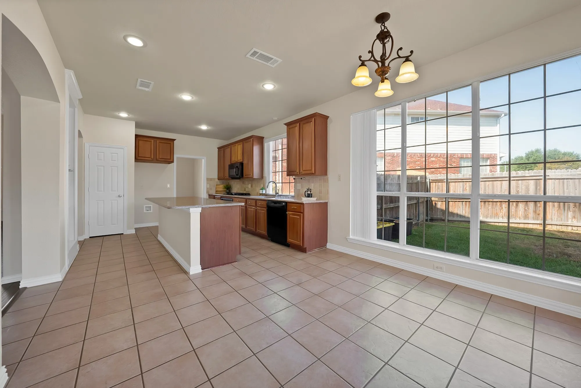 Kitchen with recessed lighting, wood cabinetry, built-in black appliances, and a central island with a light-toned countertop