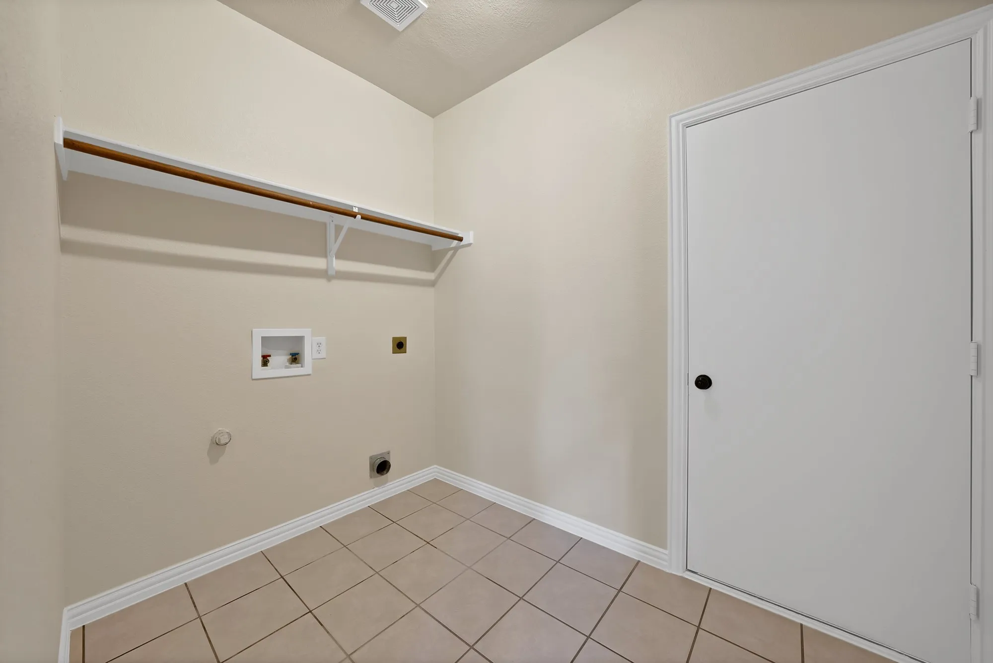 Utility space featuring a wood-finish hanging rod, neutral wall paint, white trim, and tile flooring