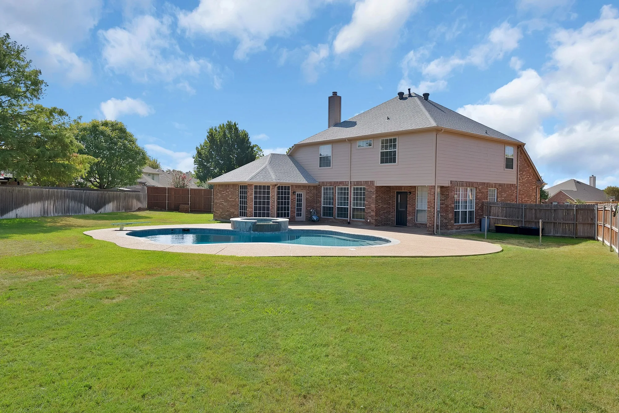 Expansive backyard featuring a large swimming pool with integrated spa, concrete decking, and a spacious lawn