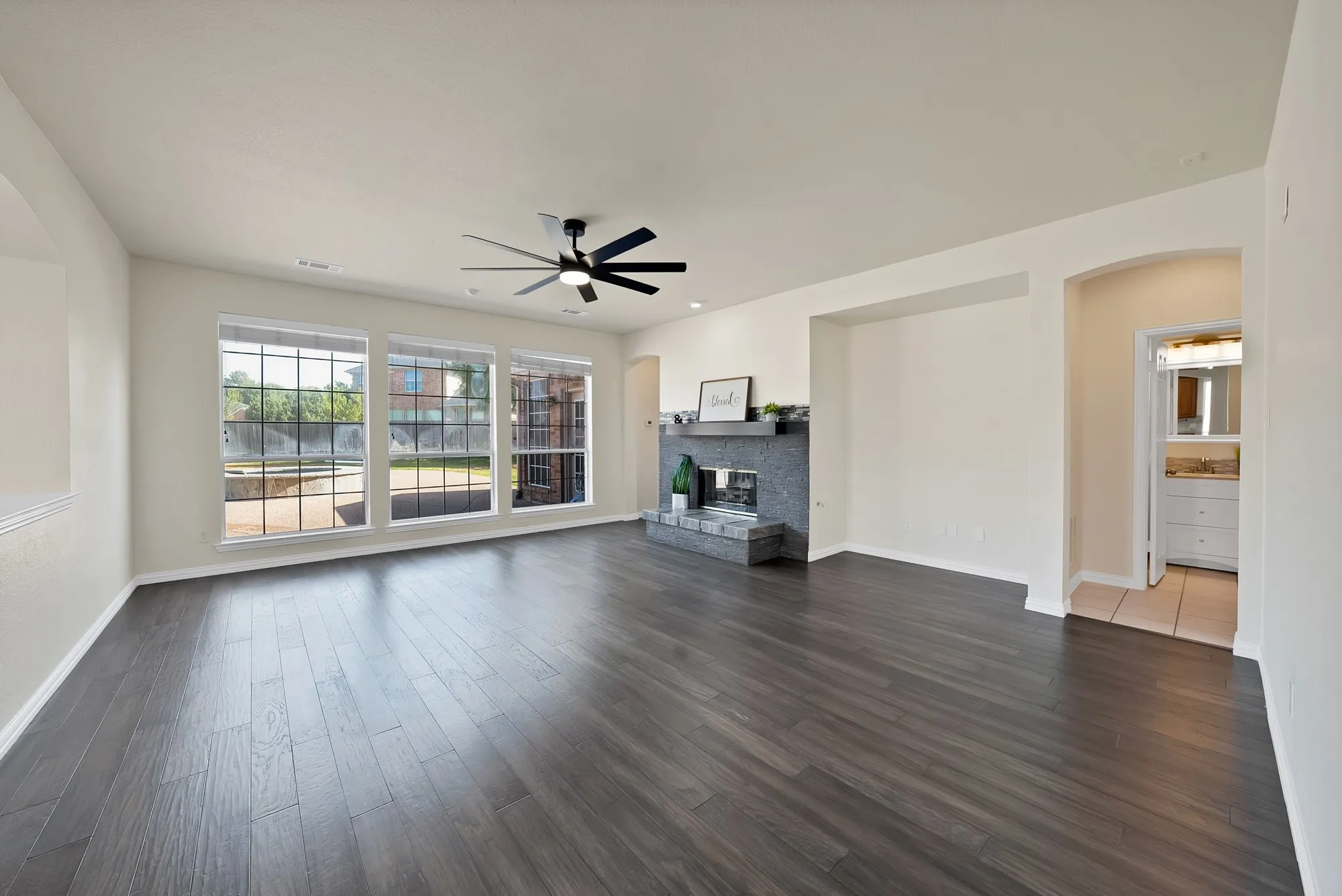 Wood-finish flooring, built-in fireplace, modern ceiling fan, arched doorway, and multiple windows