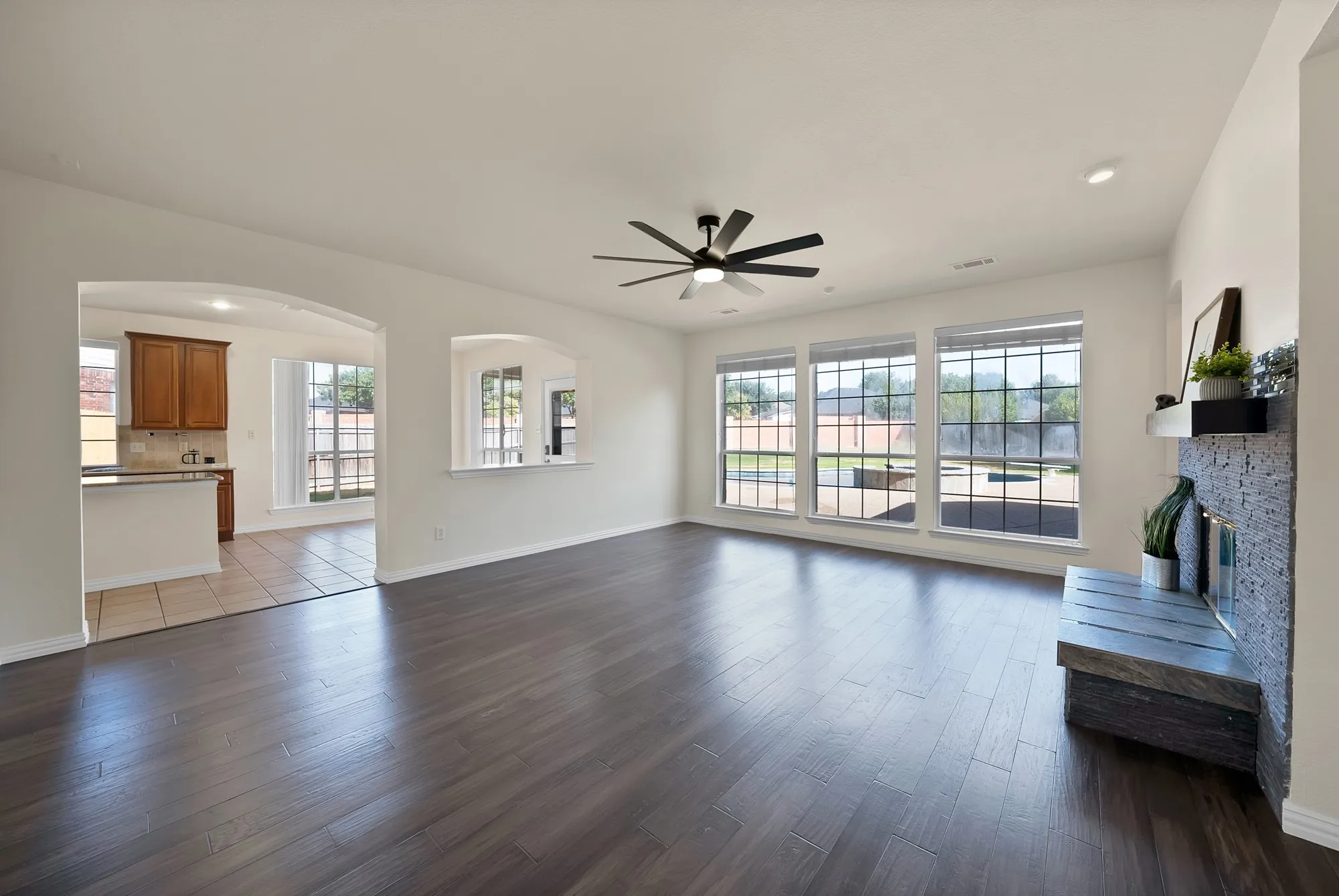 Spacious room with wood-finish flooring, a contemporary ceiling fan, and a stone-clad fireplace
