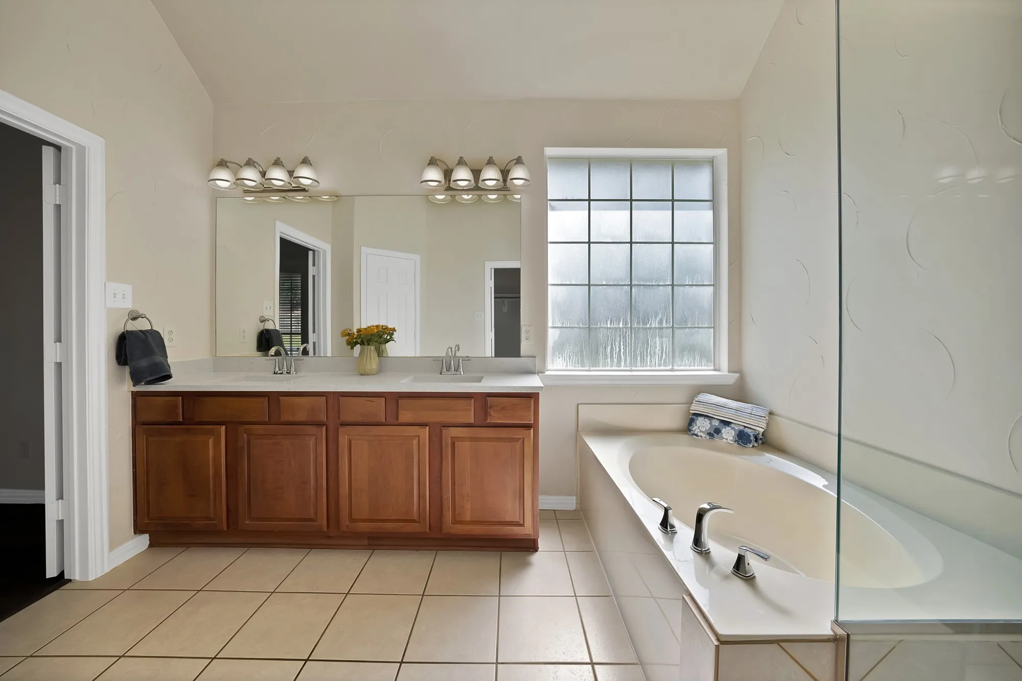 Dual vanity with wood-finish cabinetry, built-in soaking tub, and privacy window with grid pattern