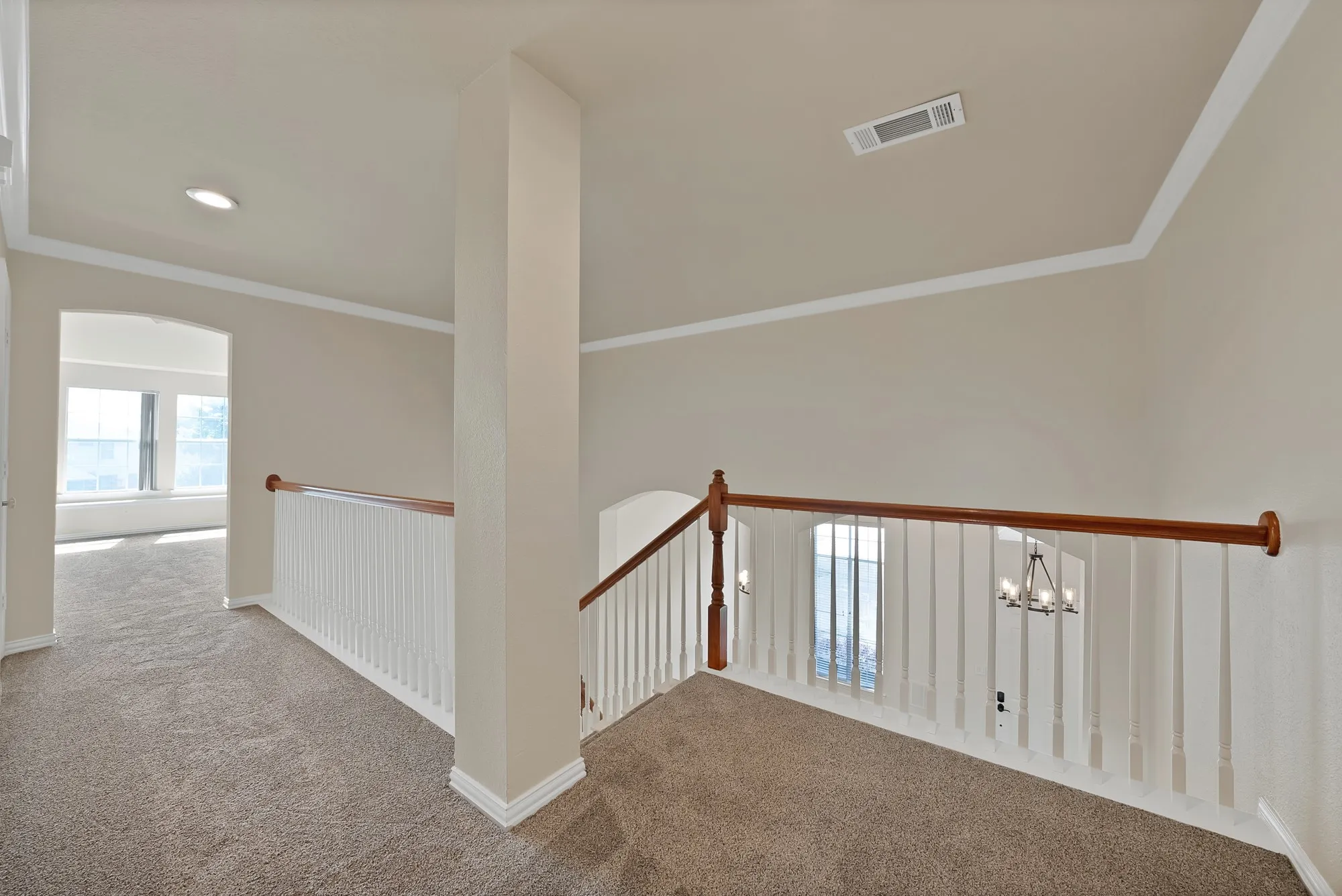 Carpeted hallway with wood-finish handrail, white balusters, and crown molding