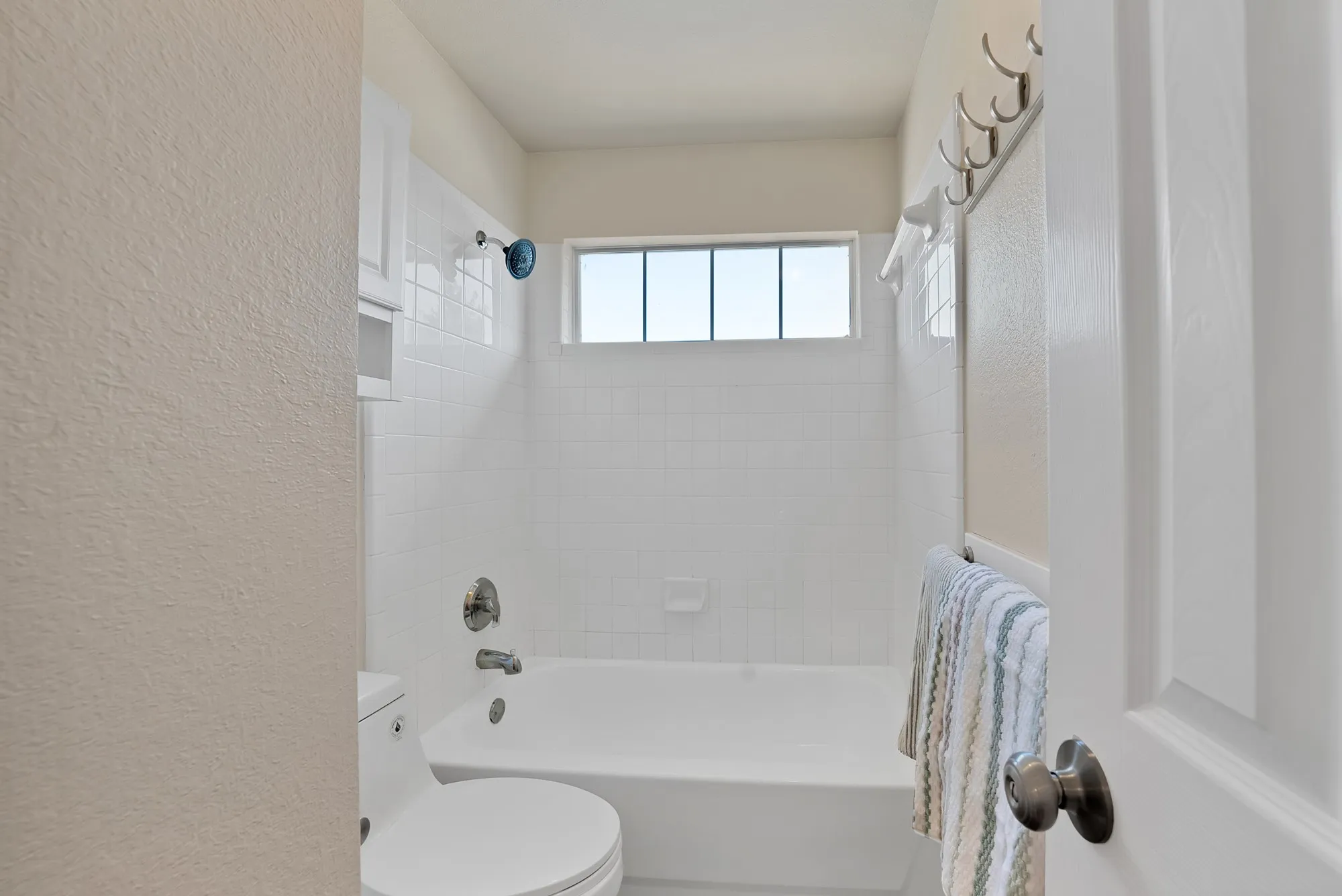 White tiled shower and tub combination with chrome fixtures and a high transom window