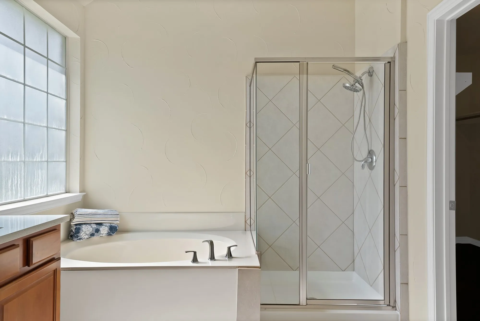 Built-in tub with dark-finish fixtures, glass-enclosed shower with tiled walls, and a window with privacy glass