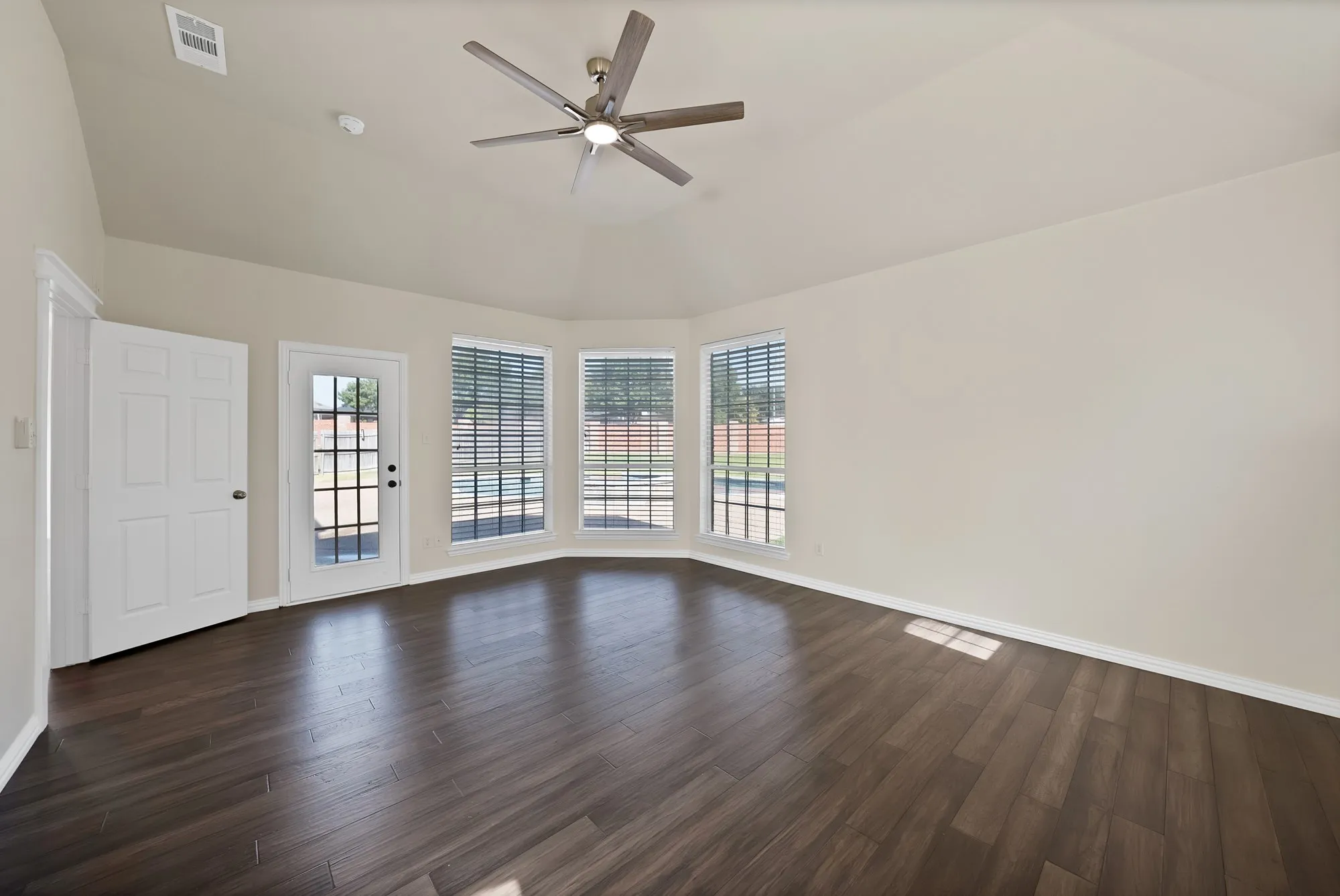 Vaulted ceiling with a ceiling fan, dark wood-finish flooring, and multiple windows with blinds