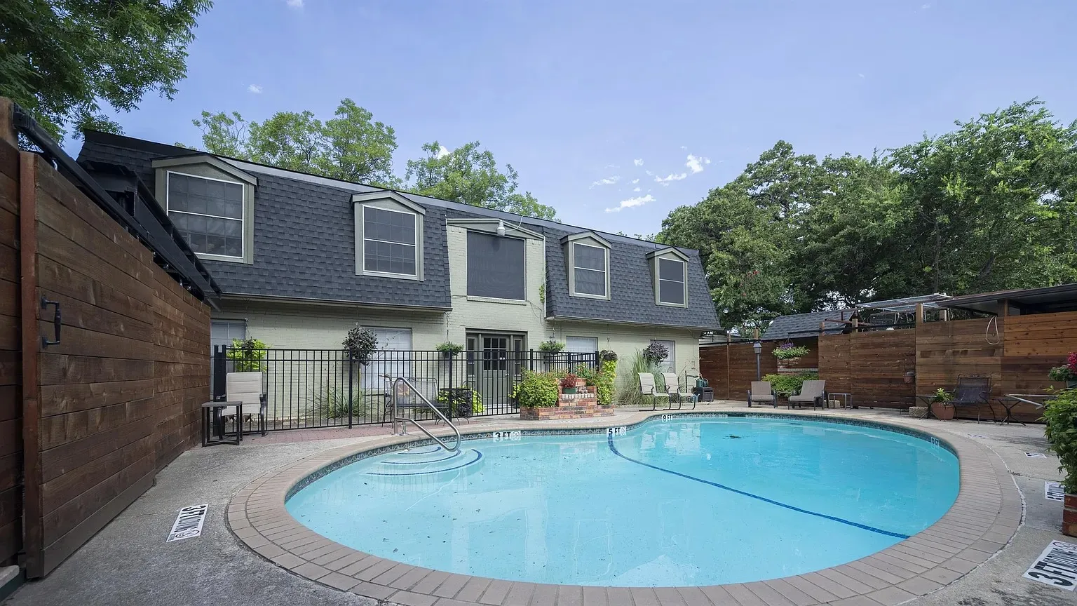 Oval-shaped swimming pool with concrete decking, surrounded by a wrought-iron fence and wood privacy fencing
