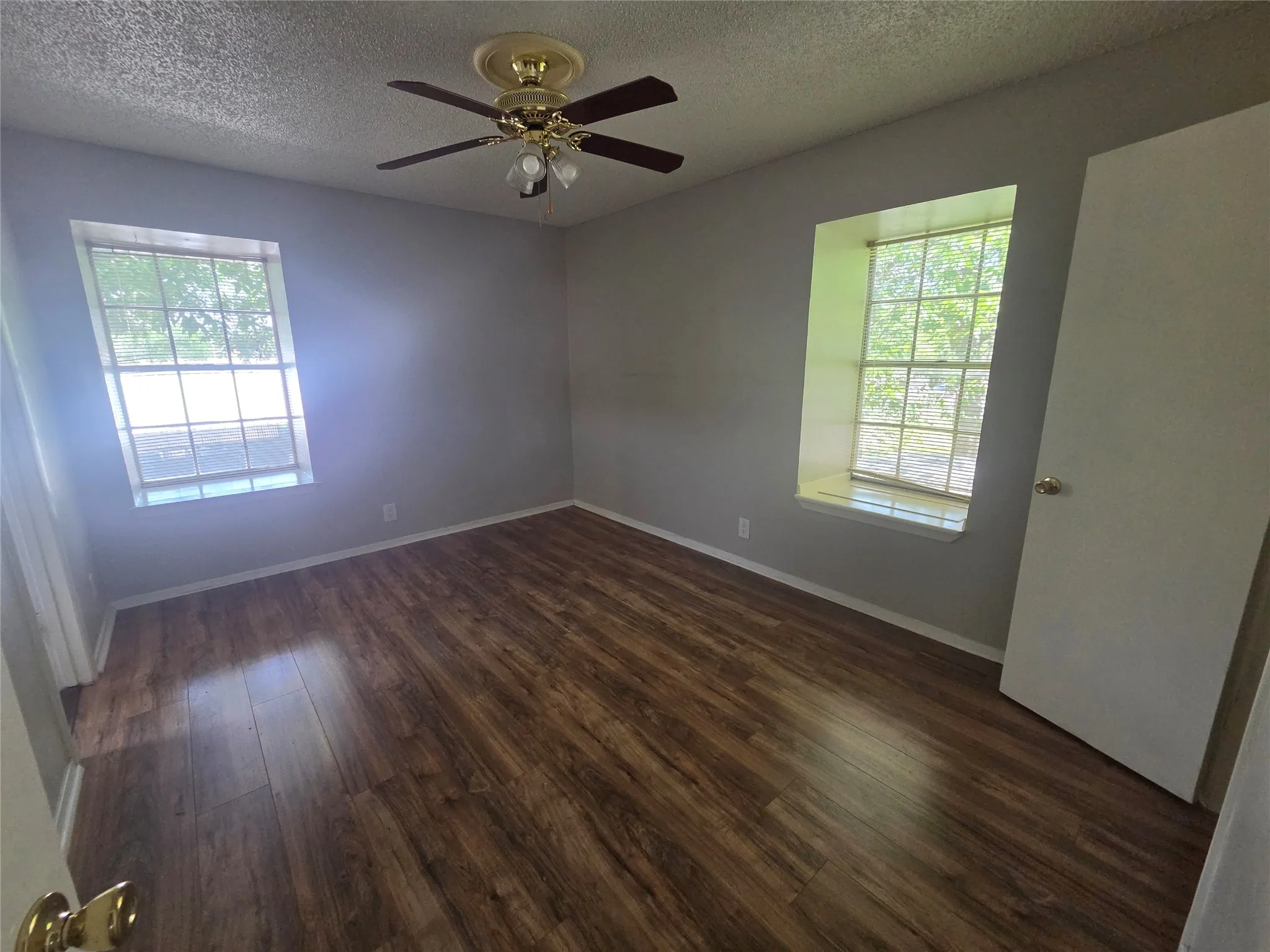 Wood-finish flooring with a ceiling fan light fixture and two windows