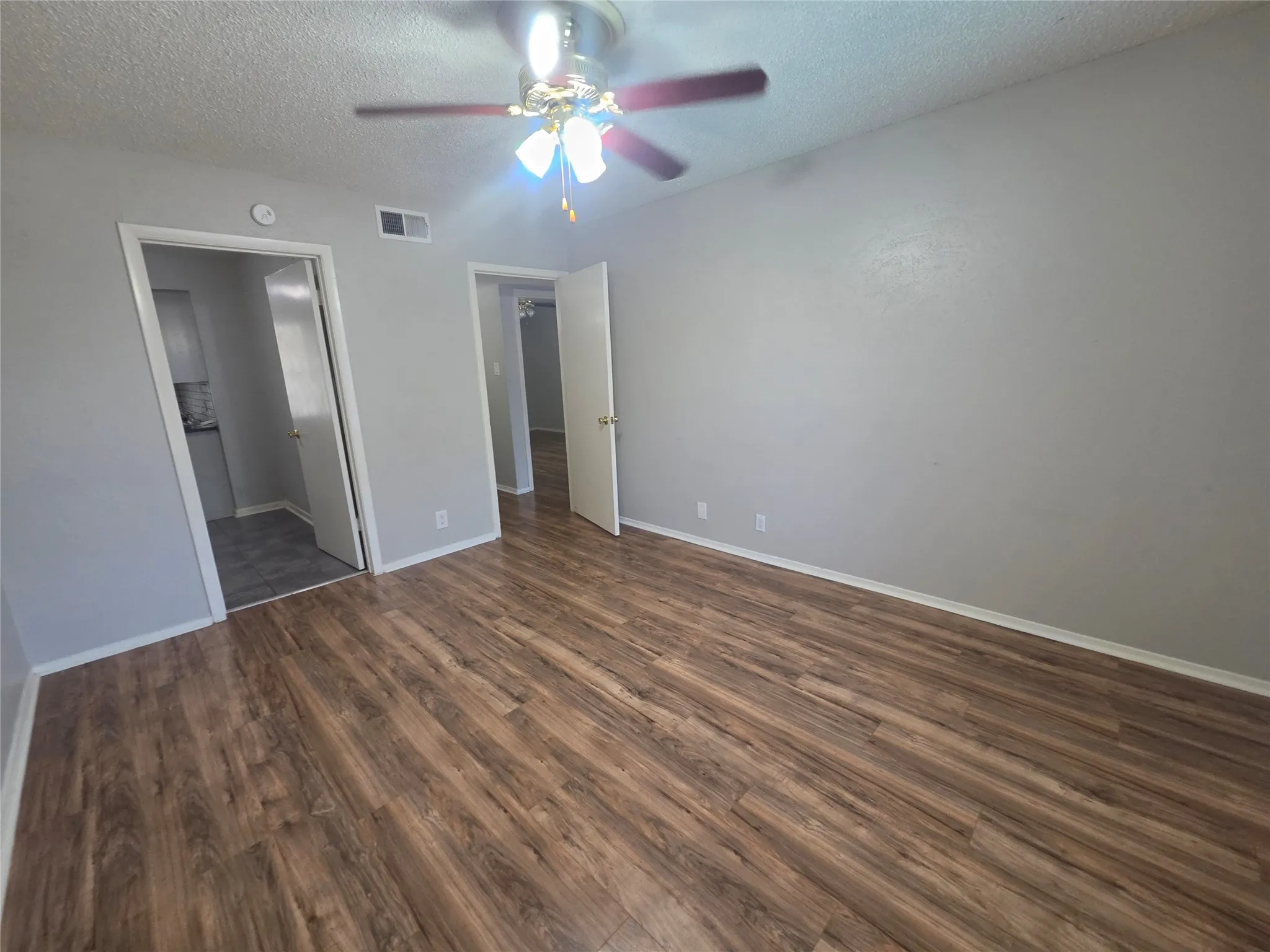 Wood-finish flooring, light gray wall finishes, and a ceiling fan with integrated lighting