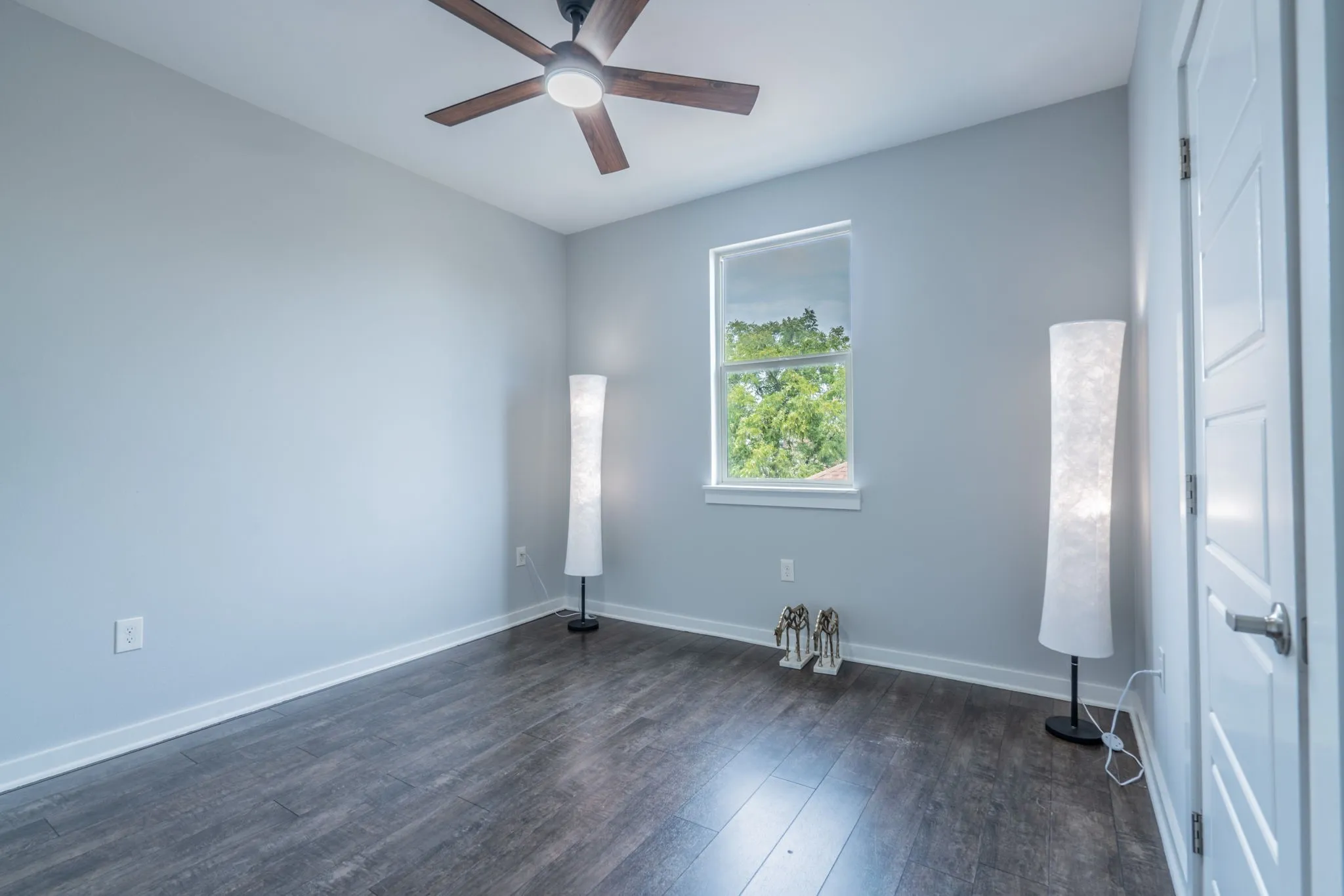 Ceiling fan with integrated lighting, wood-finish flooring, single window, and a paneled interior door