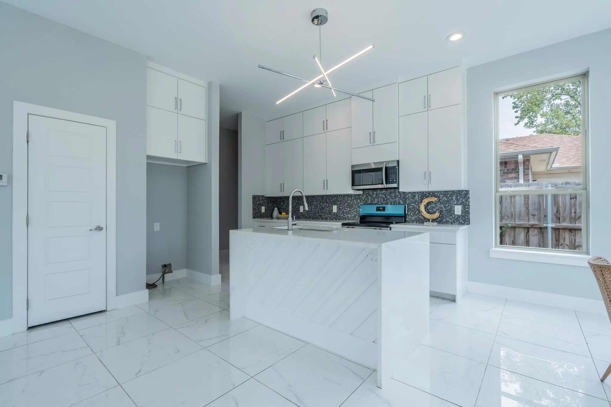 Kitchen featuring white cabinetry, a central island with a waterfall edge, stainless steel appliances, and large format floor tiling