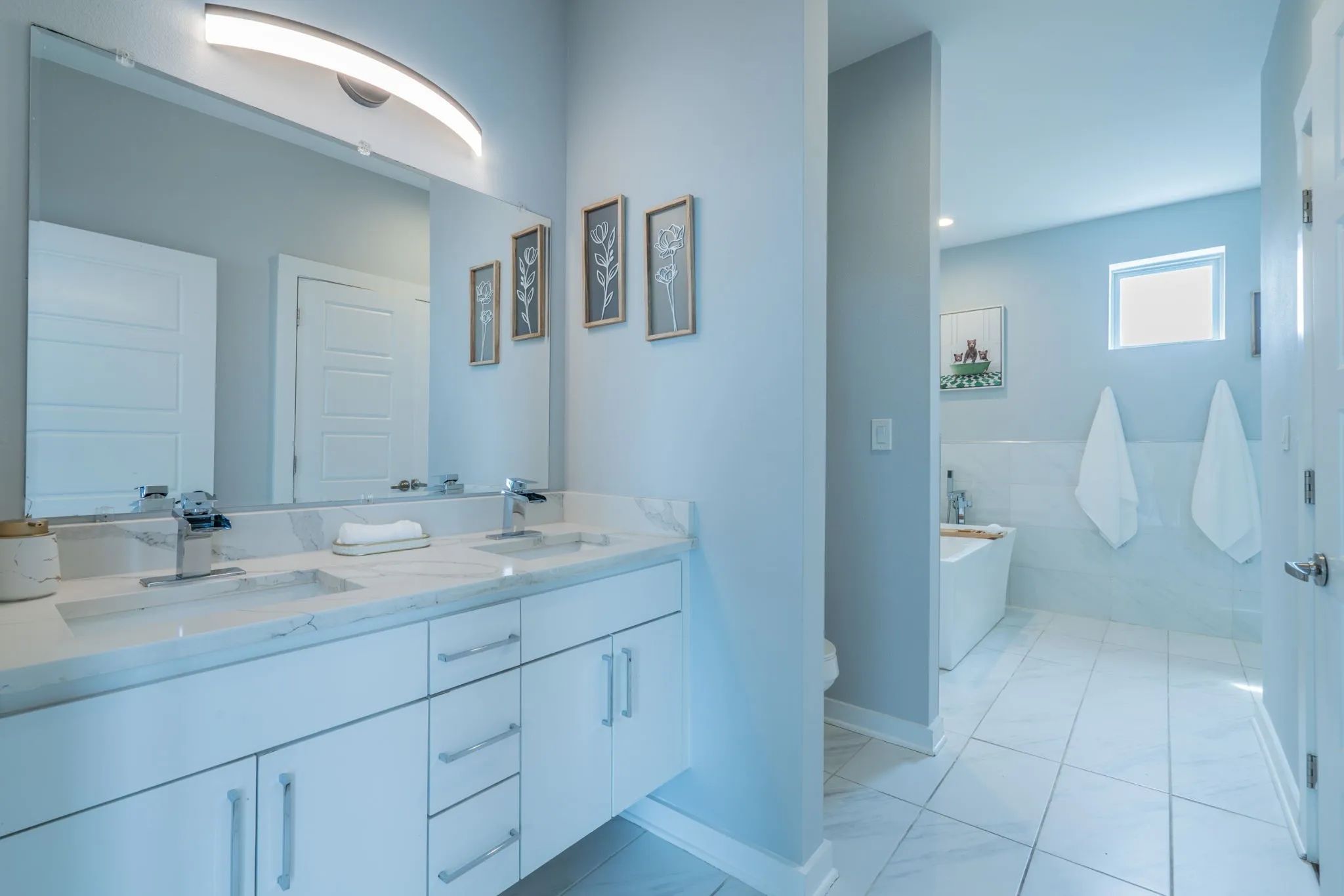 Dual vanity with white cabinetry and chrome hardware, featuring a large mirror and countertop with integrated sinks