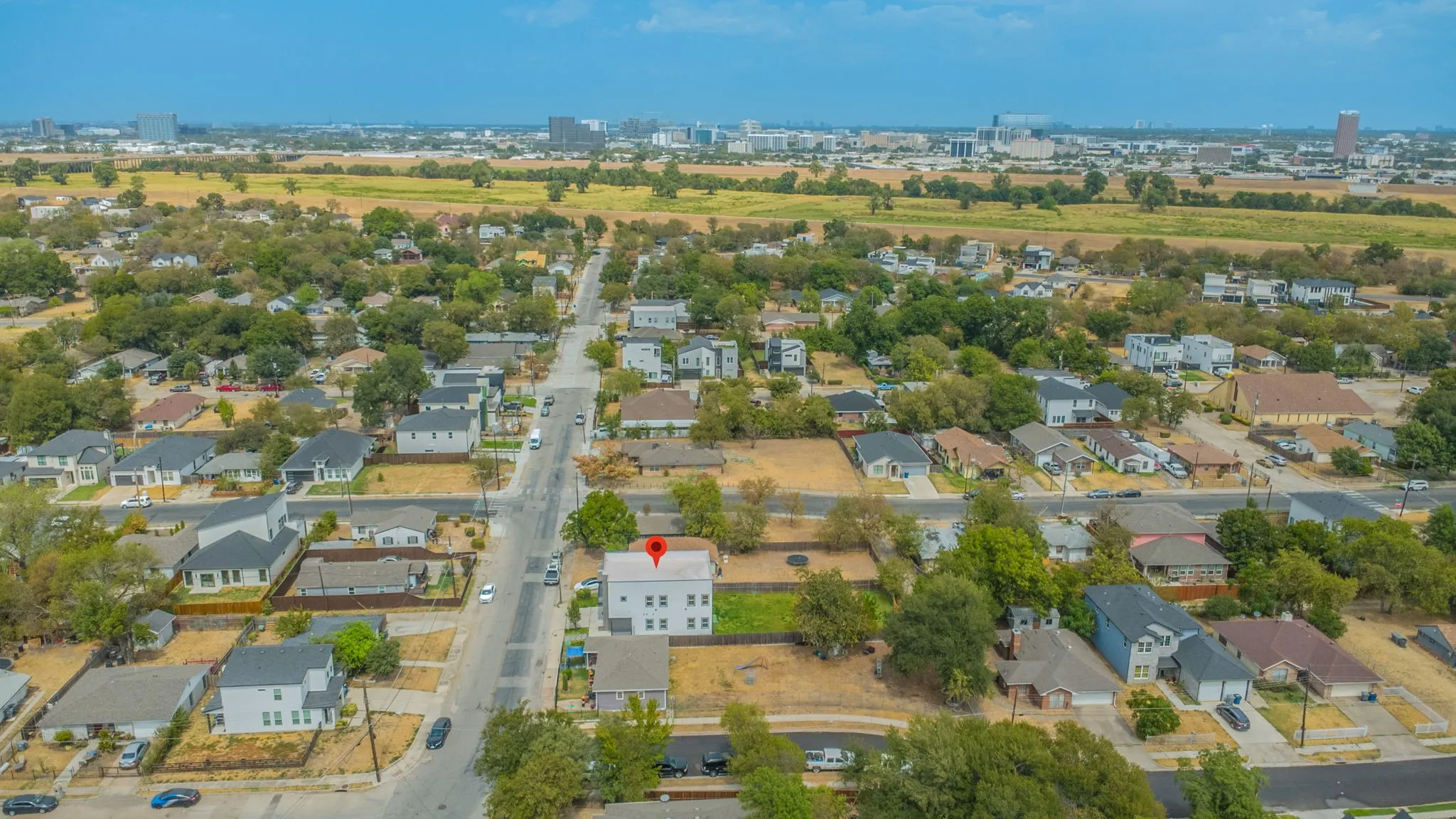 Aerial perspective of a residential neighborhood with mixed architectural styles, mature trees, and a distant city skyline