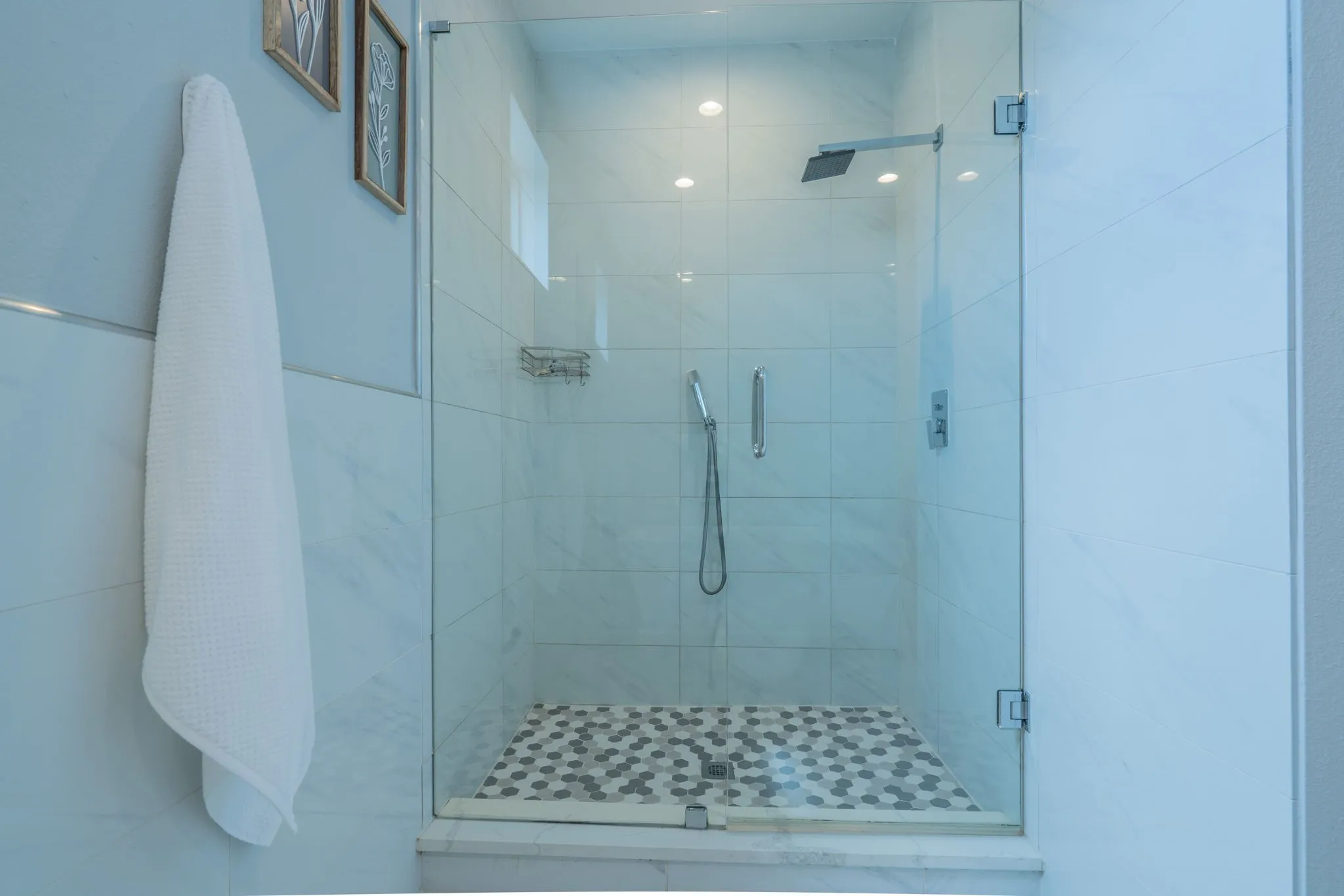 Glass-enclosed shower with a rainfall showerhead, handheld sprayer, and mosaic tile flooring