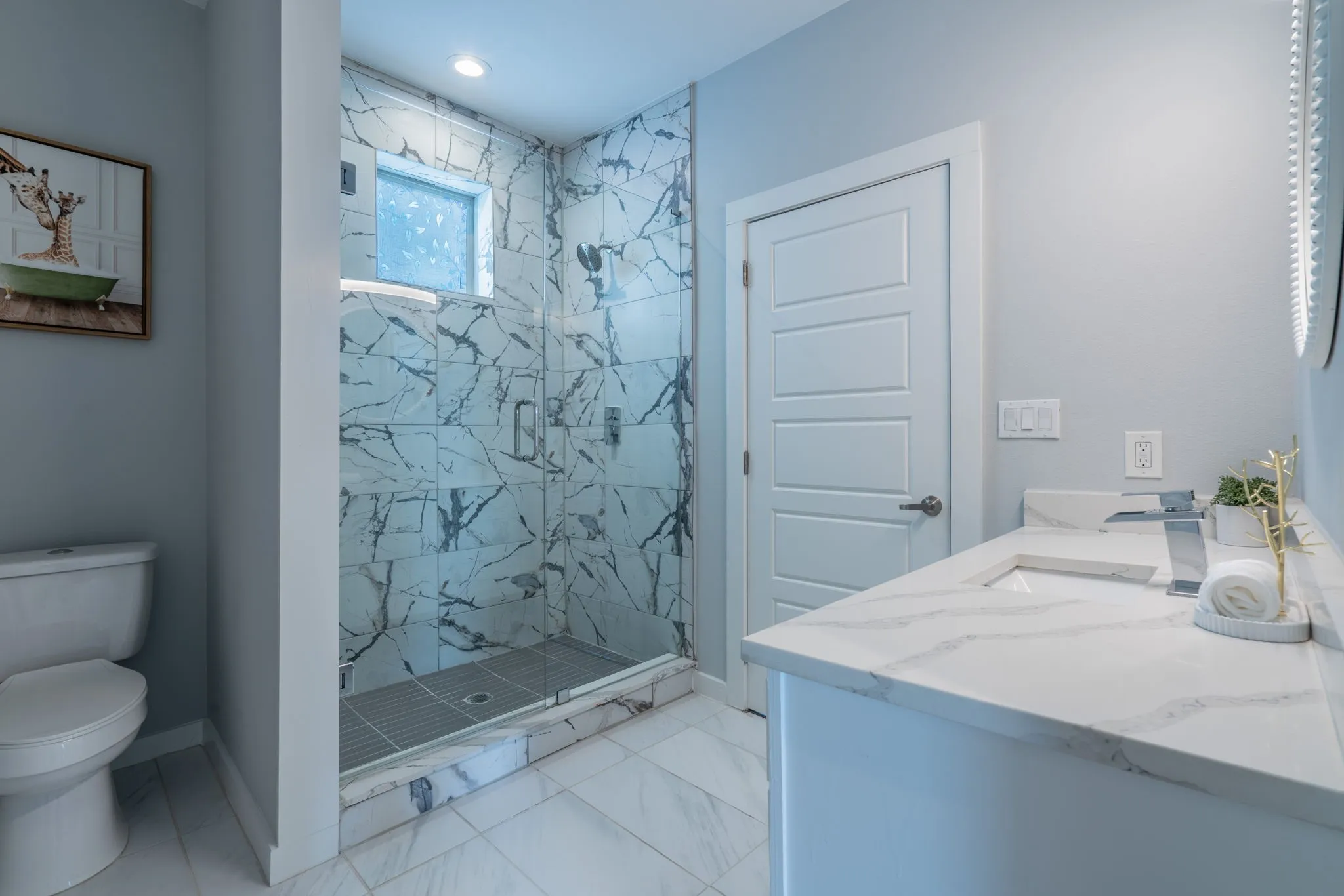 Walk-in shower with full-height marble-patterned tile, glass enclosure, and transom window