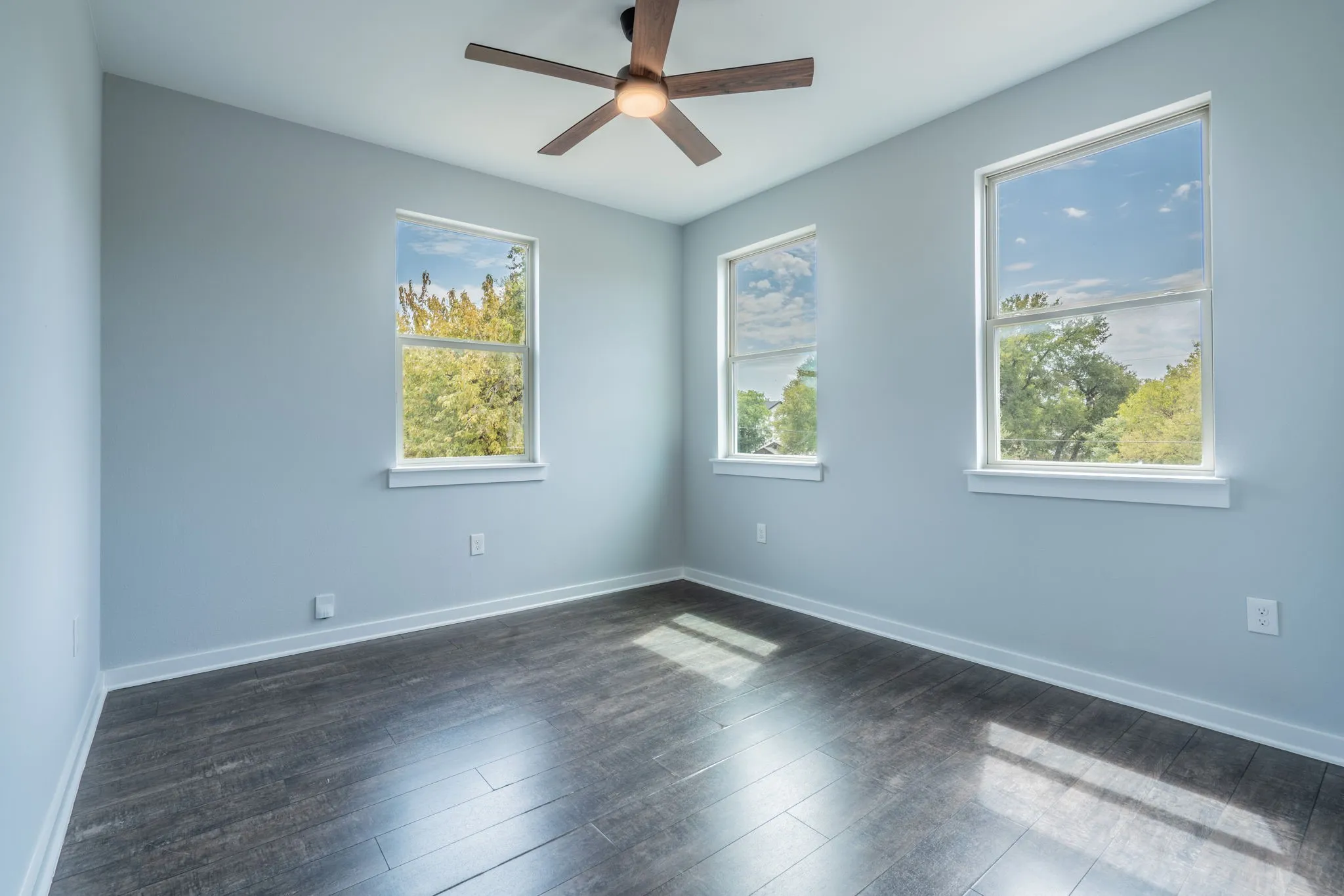 Wood-finish flooring, three double-hung windows, light-toned walls, and a ceiling fan with integrated lighting