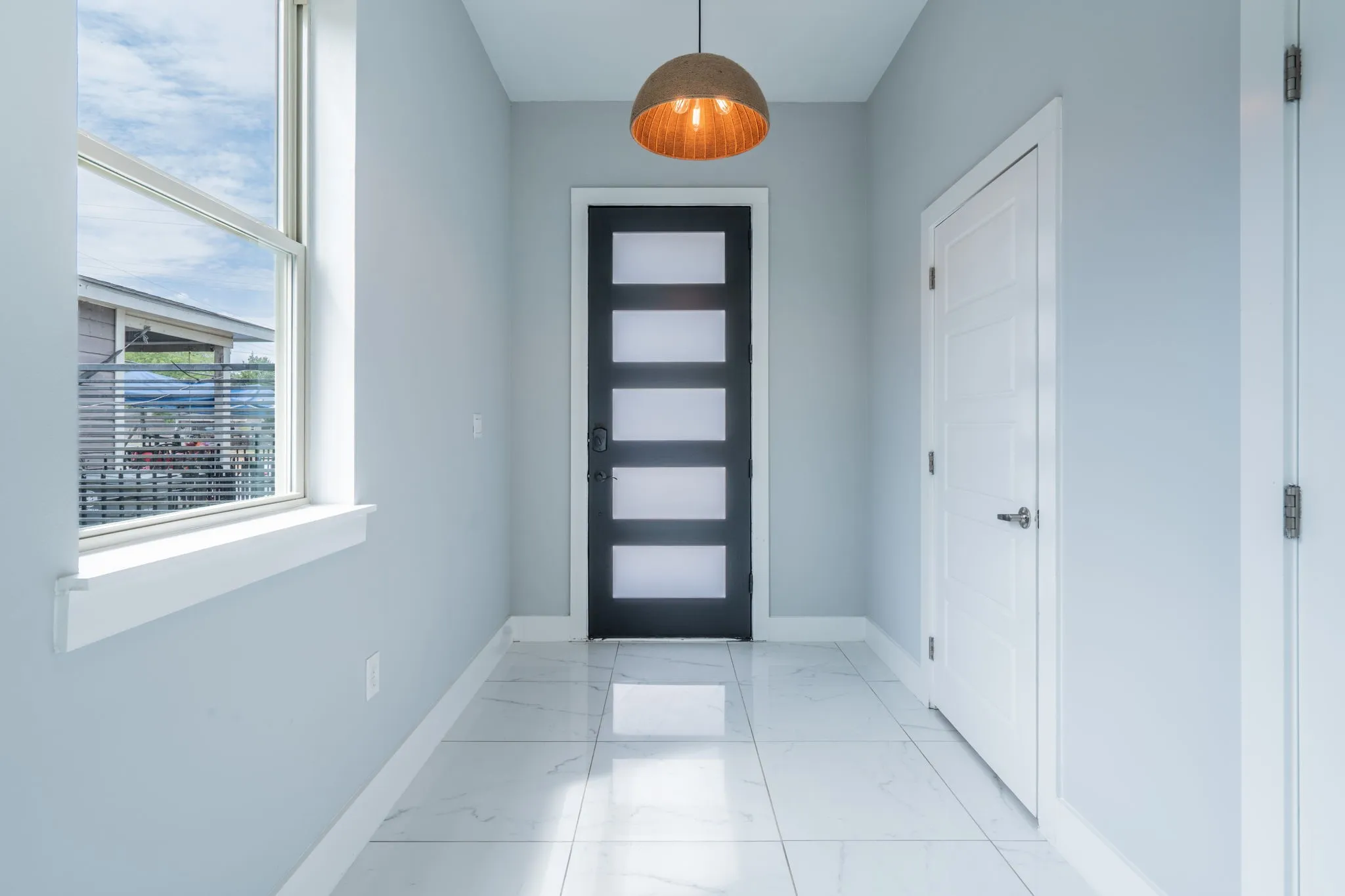 Entryway featuring large format tiled flooring, a modern front door with frosted glass panels, a pendant light fixture, and a single-hung window with white trim