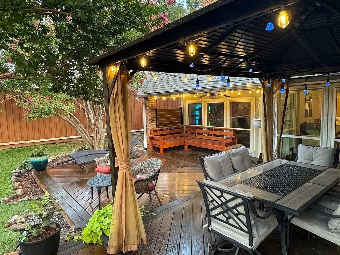 Outdoor deck featuring a black metal gazebo with string lighting, a privacy fence, and mature trees