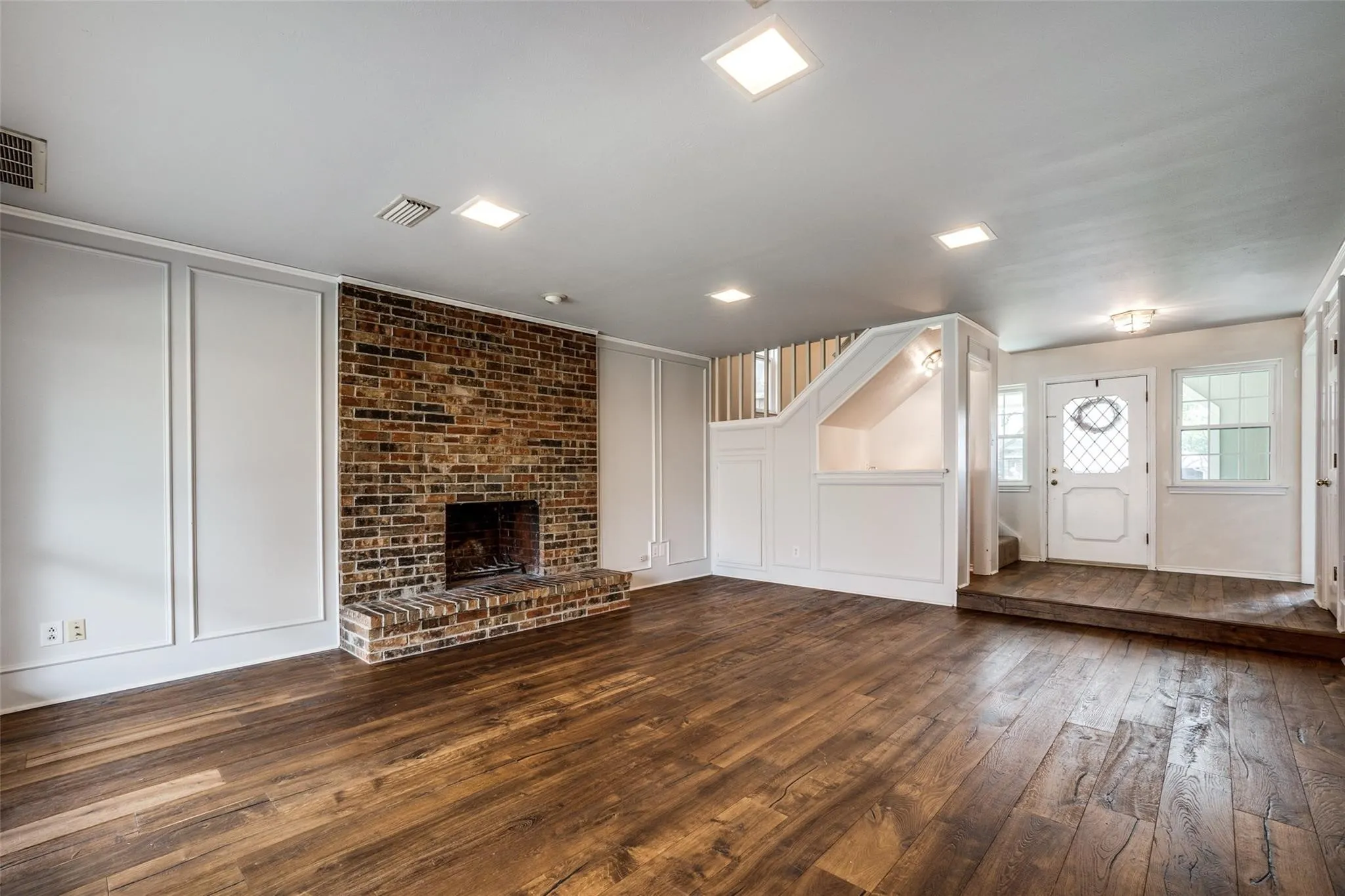 Hardwood-finish flooring, brick fireplace with hearth, recessed lighting, wall paneling, and an entry door with sidelights
