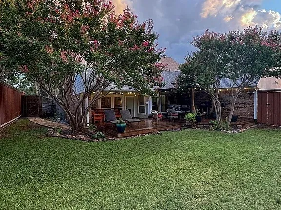 Expansive backyard with a manicured lawn, a large wood-finish deck, and mature trees
