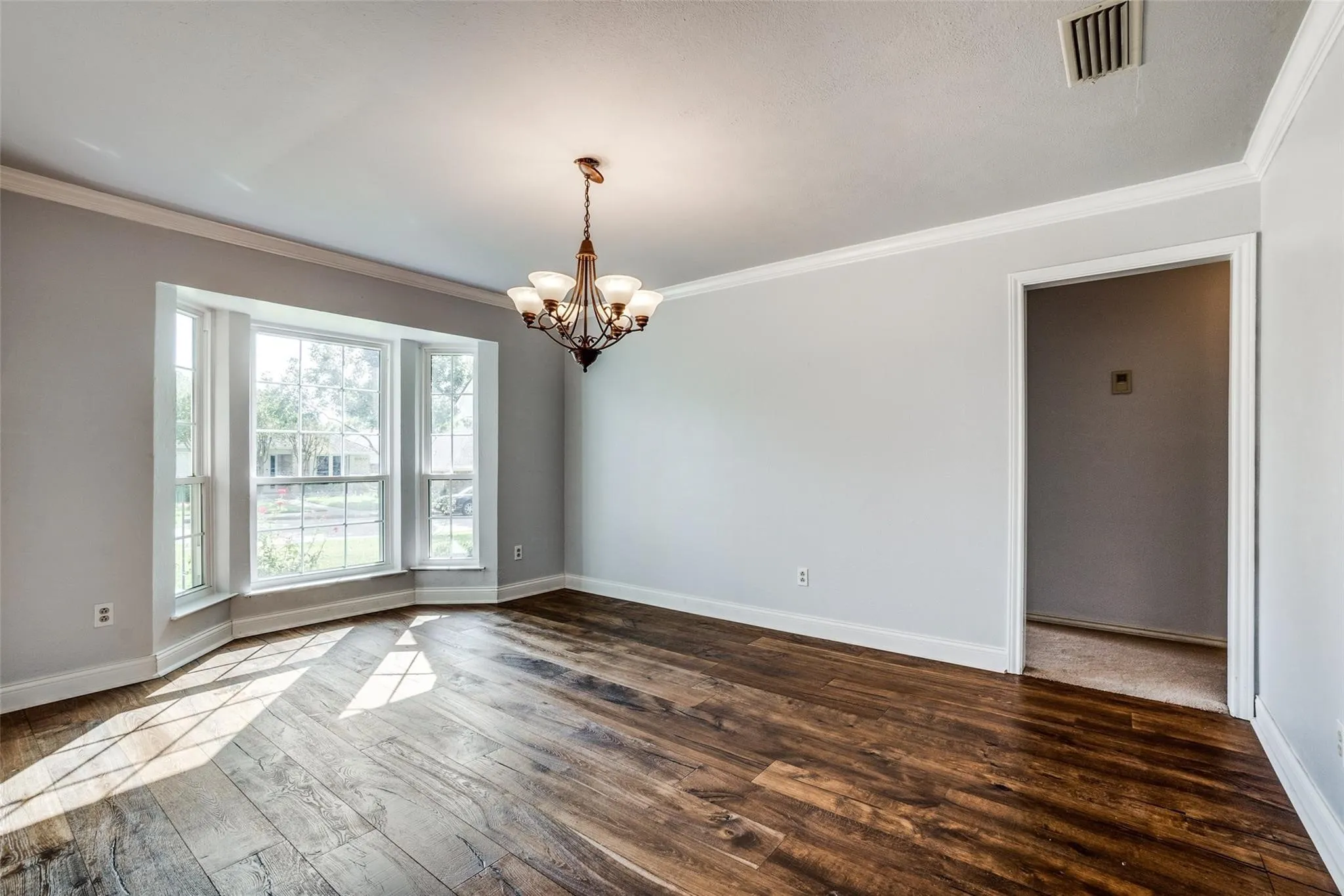 Wood-finish flooring, bay window, crown molding, and a chandelier lighting fixture