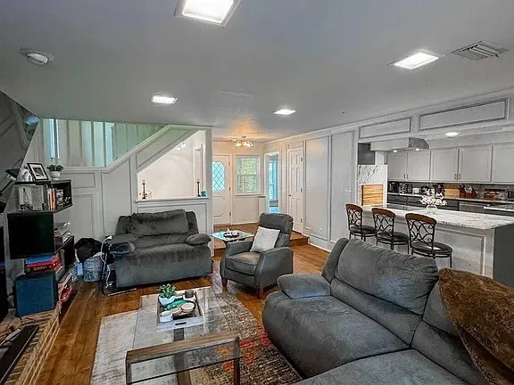Open-concept living area with wood-finish flooring, recessed lighting, and a kitchen featuring a large island with seating, integrated appliances, and panel cabinetry