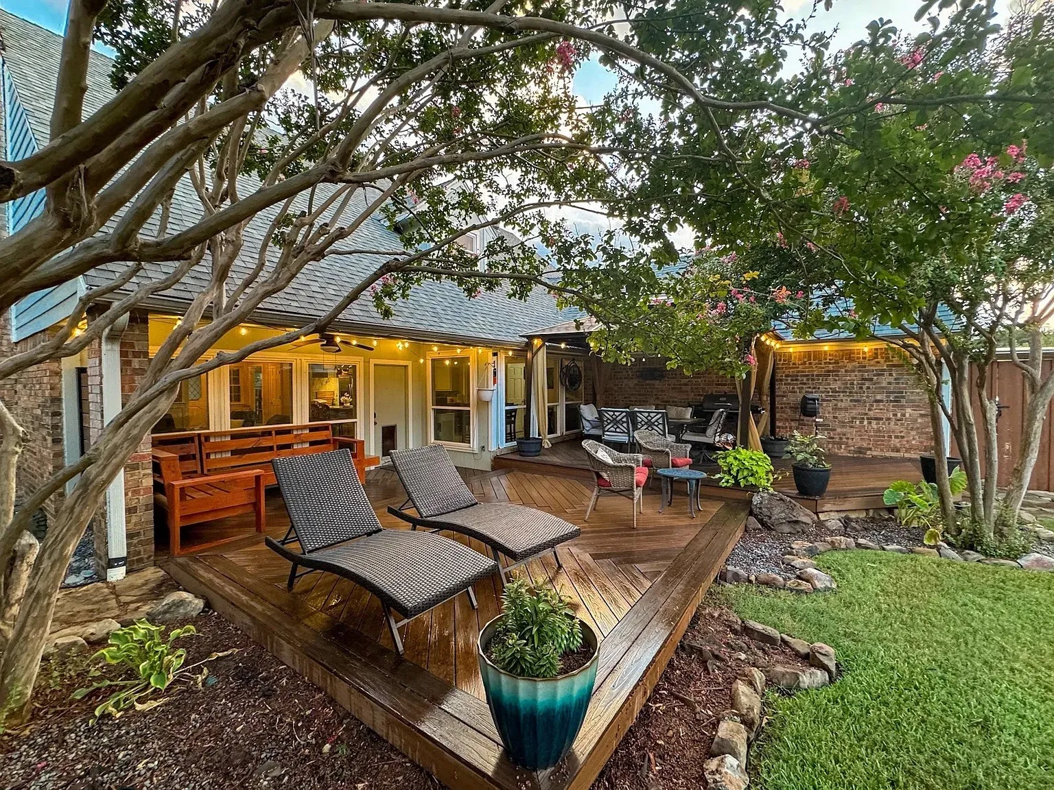 Expansive wood-finish deck with integrated lighting, surrounded by mature trees and manicured landscaping
