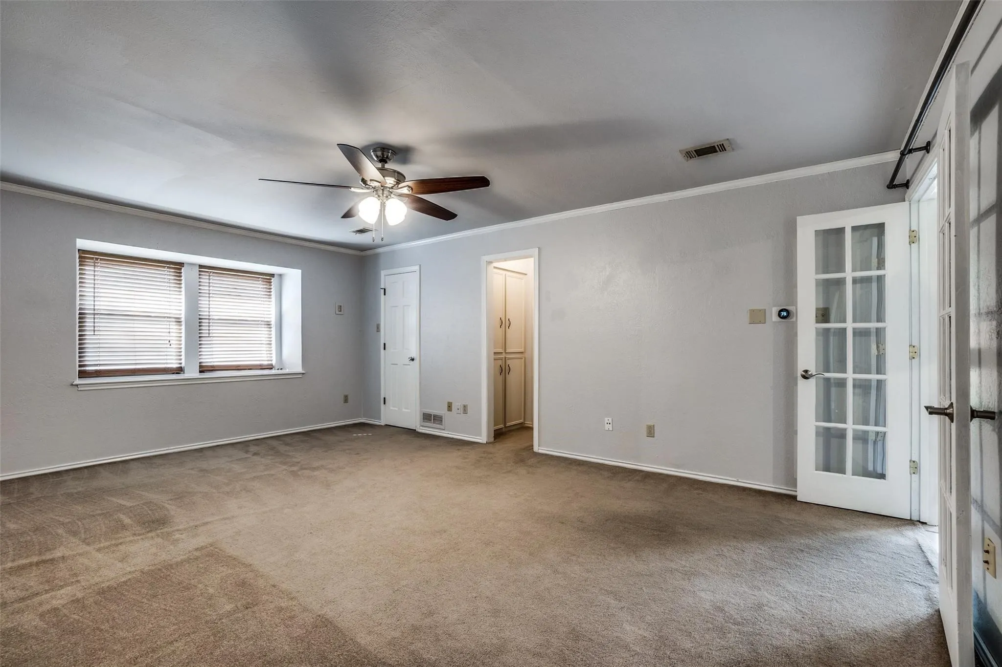 Spacious room featuring neutral carpeting, a ceiling fan, and crown molding