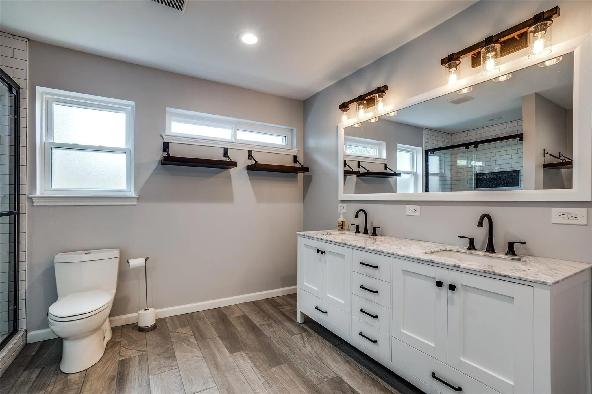 Dual vanity with white cabinetry and dark hardware, set under a large framed mirror with industrial-style lighting