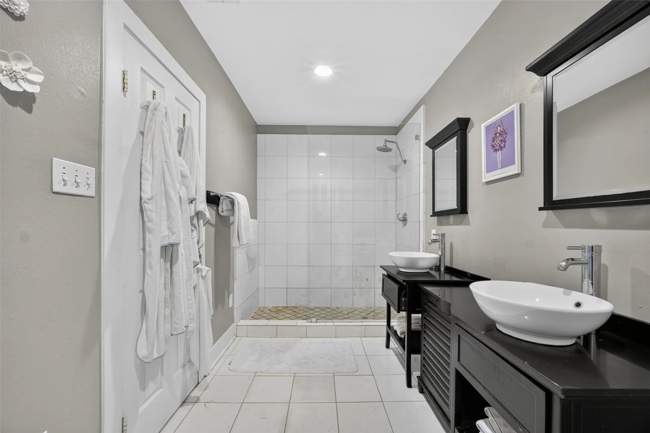 Spa-inspired primary bathroom featuring a walk-in shower with subway tile surround, dual vanities with vessel sinks and matte black hardware, recessed ceiling lighting, and neutral tile flooring​​‌​​​​‌​​‌‌​‌‌​​​‌‌​‌​‌​‌​​​‌​​ throughout