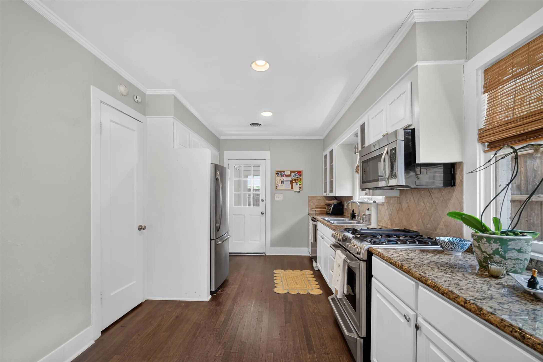 Kitchen featuring wood-finish flooring, white cabinetry, a built-in stainless steel microwave, and granite countertops