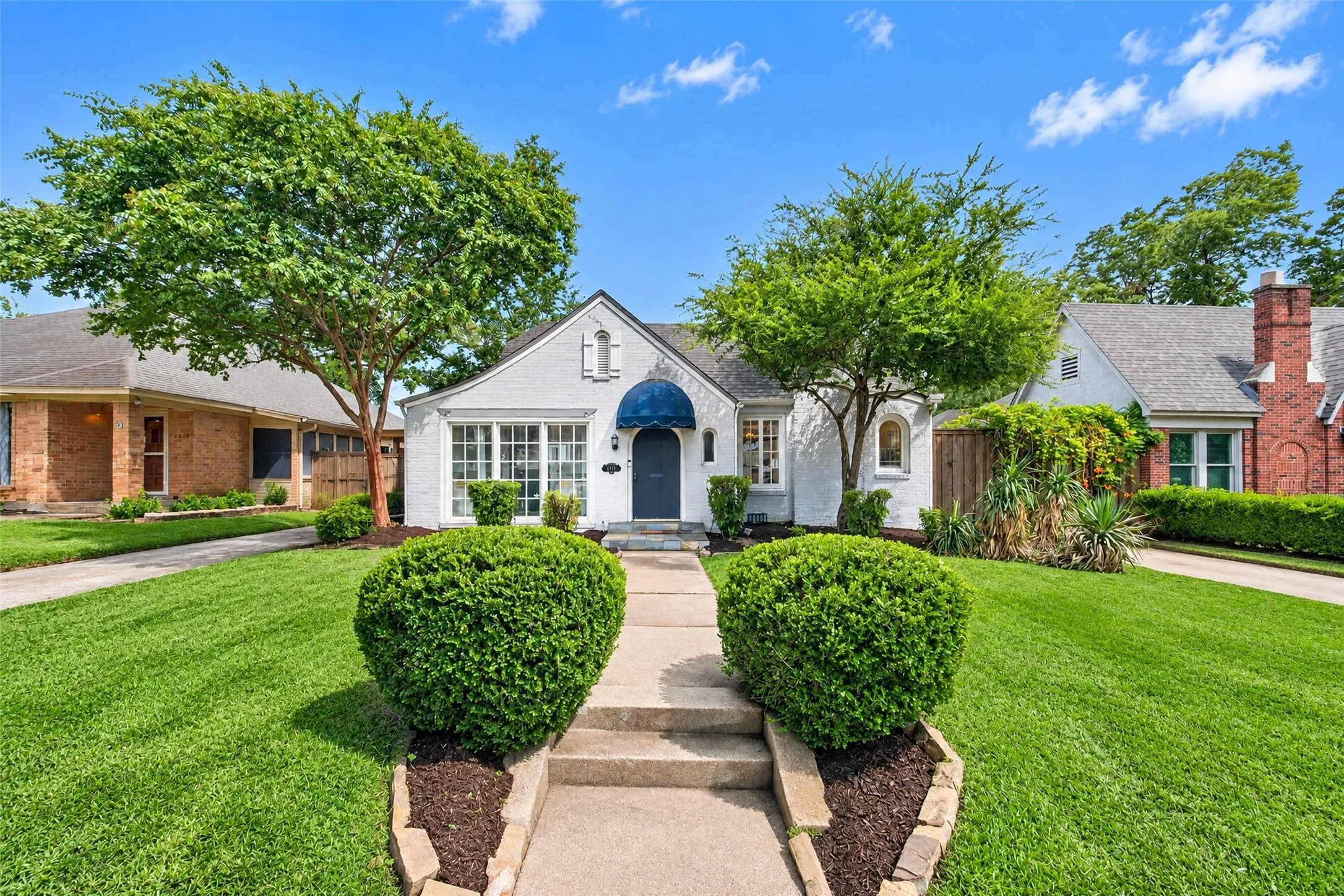 White stucco exterior with a dark blue awning, multiple paned windows, and a concrete pathway