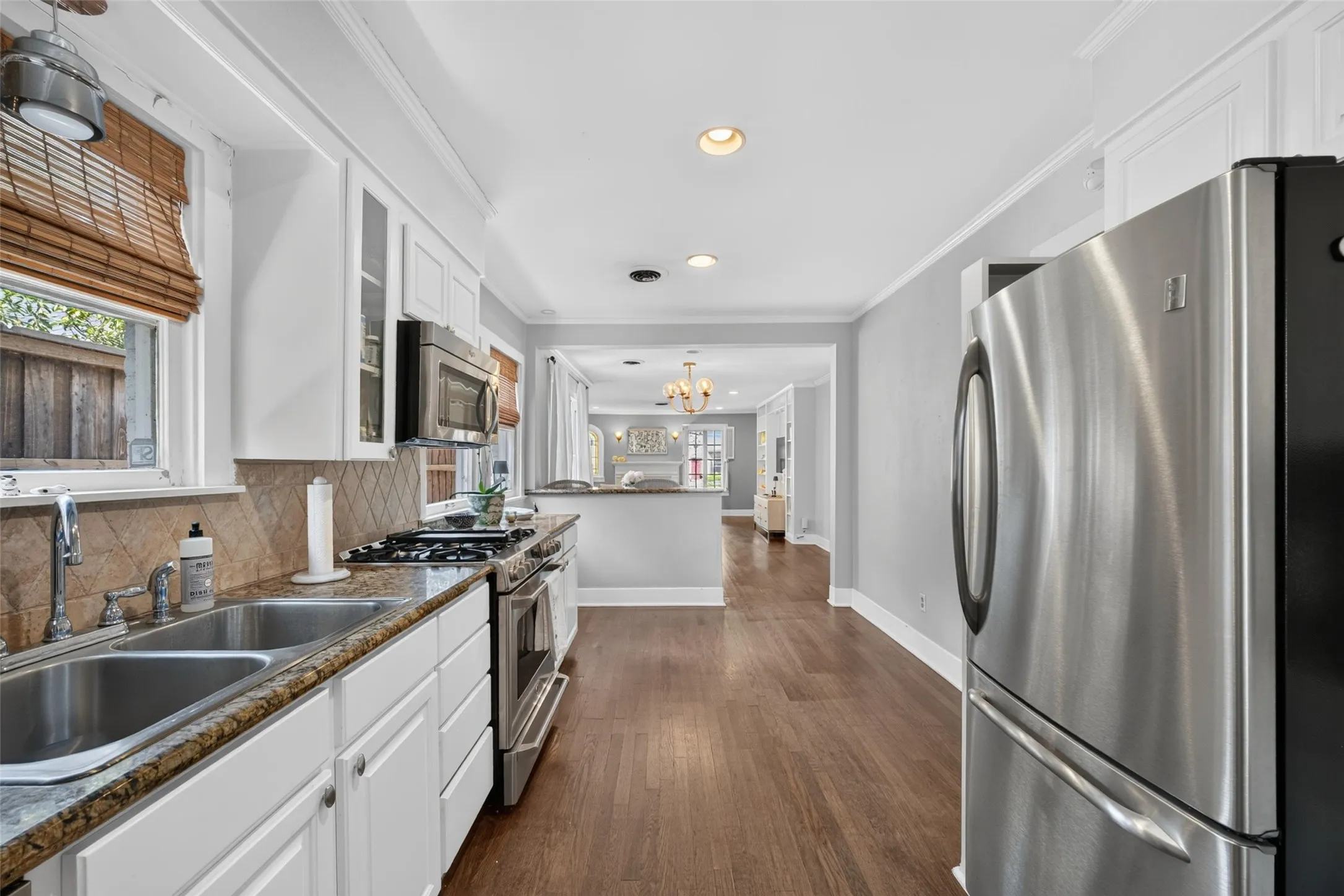 Stainless steel appliances, wood-finish flooring, white cabinetry, integrated double basin sink, and recessed lighting