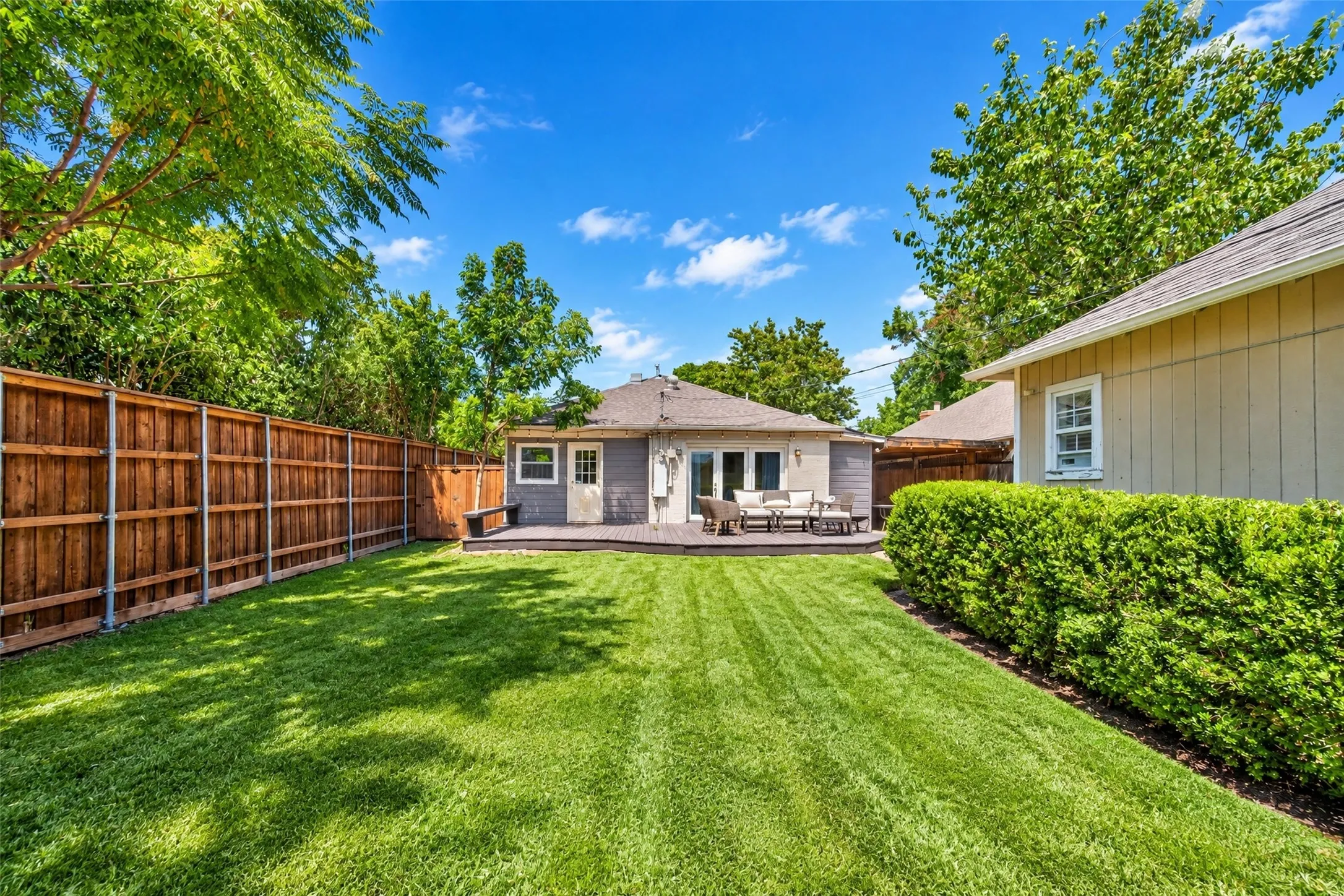 Expansive backyard featuring a manicured lawn, wood privacy fencing, and mature trees