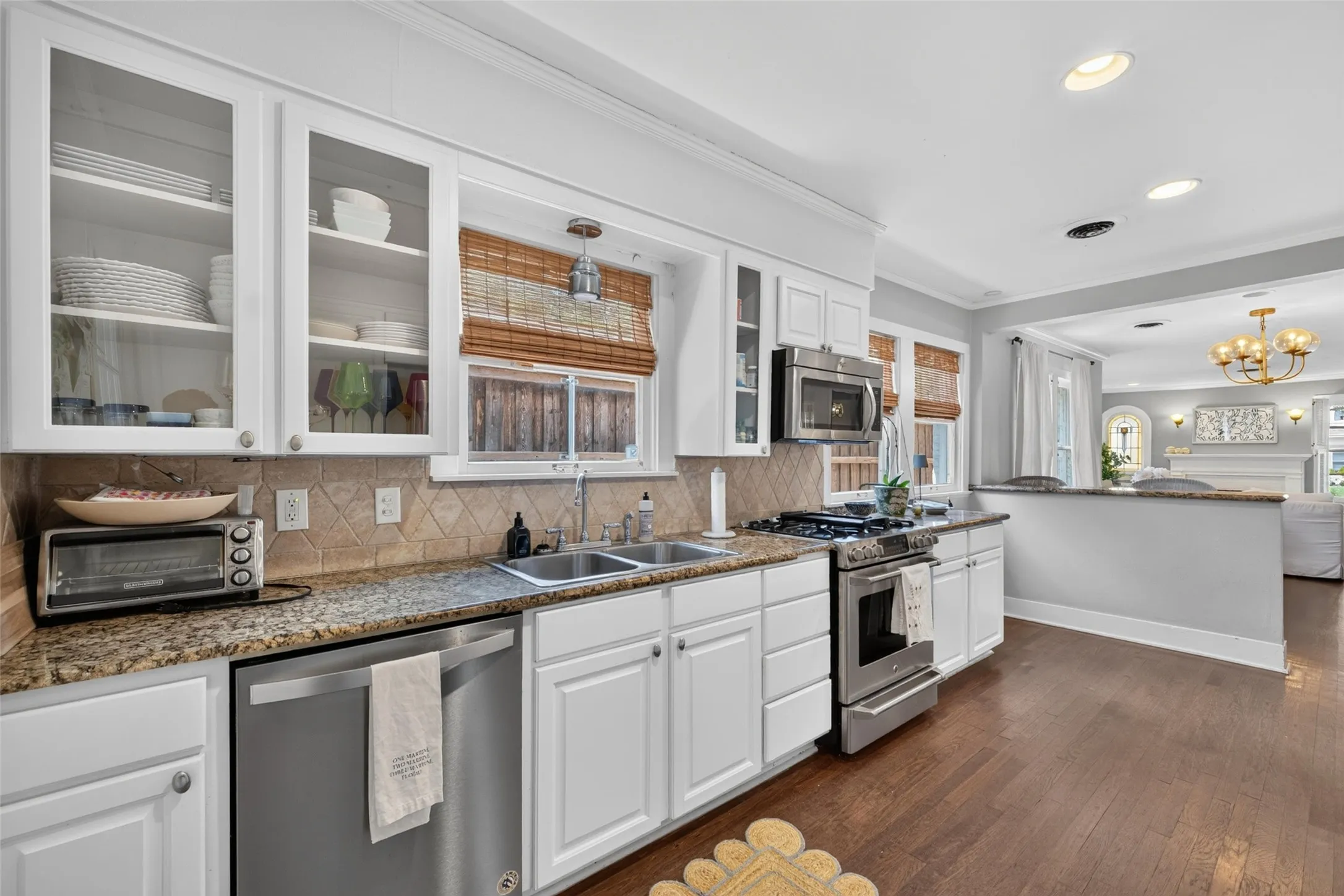 White cabinetry with glass-front uppers, stainless steel appliances, granite countertops, and wood-finish flooring