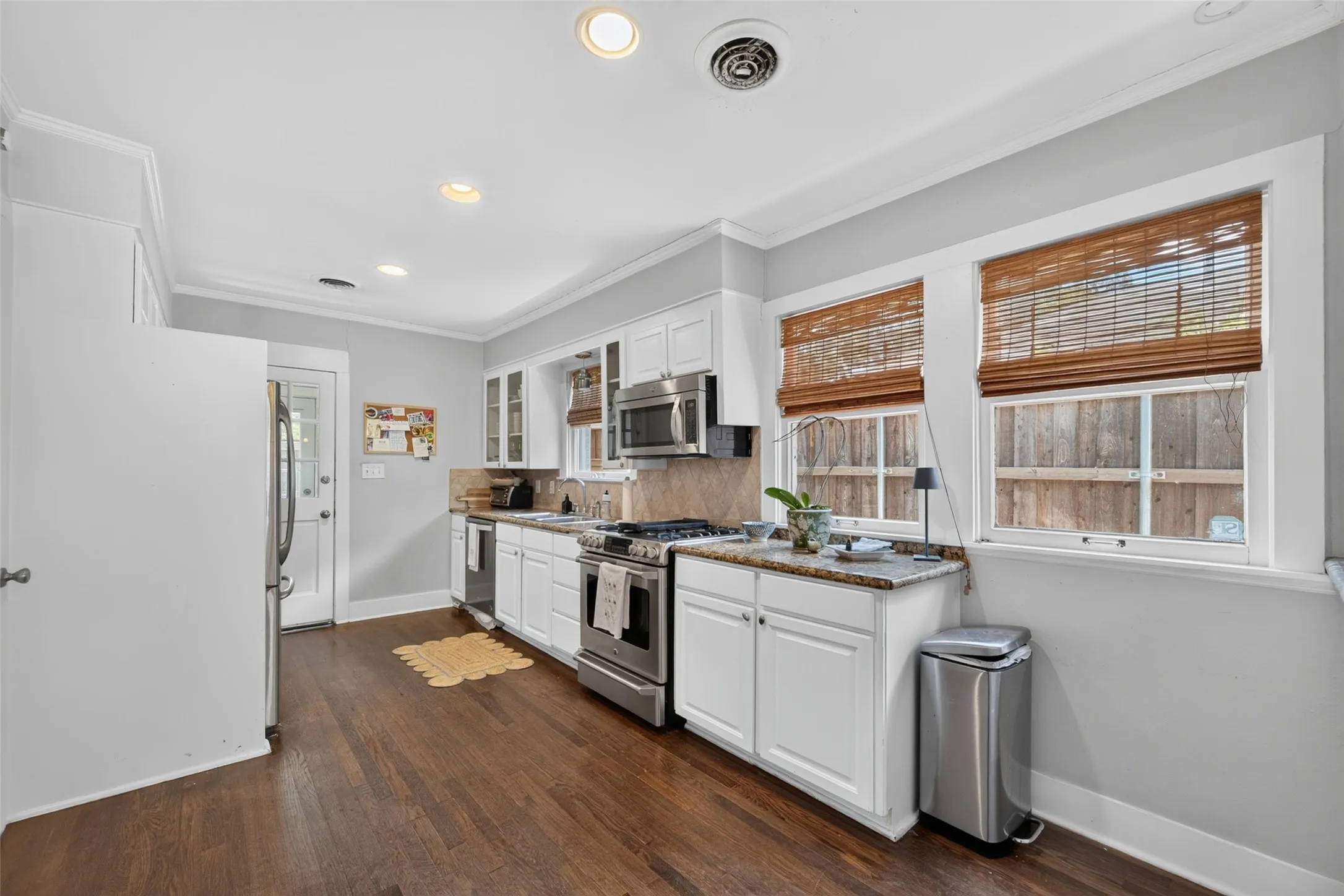 White cabinetry with stainless steel appliances, wood-finish flooring, recessed lighting, and crown molding