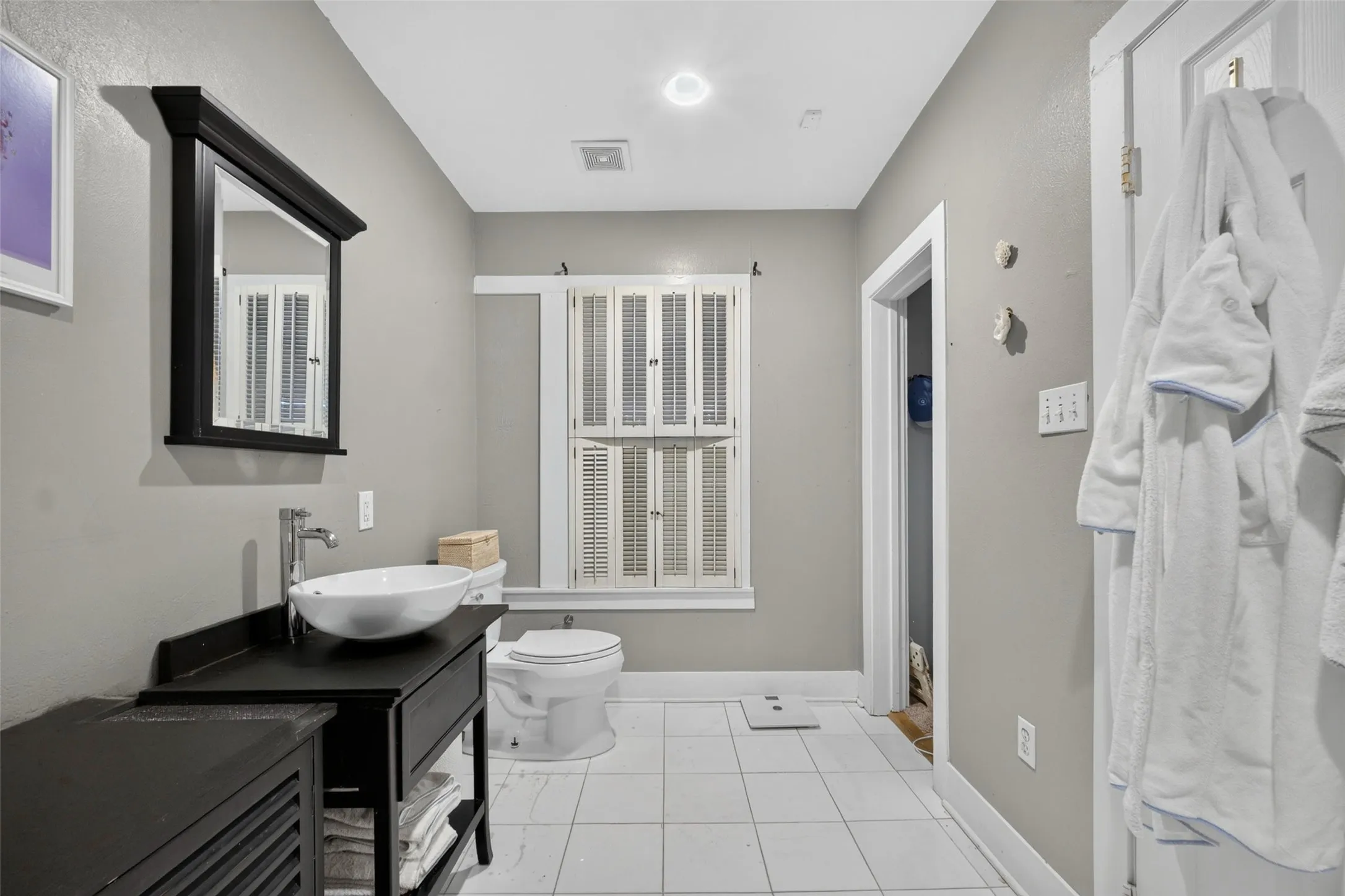 White vessel sink with chrome faucet, black vanity with open shelving, recessed lighting, and white tile flooring